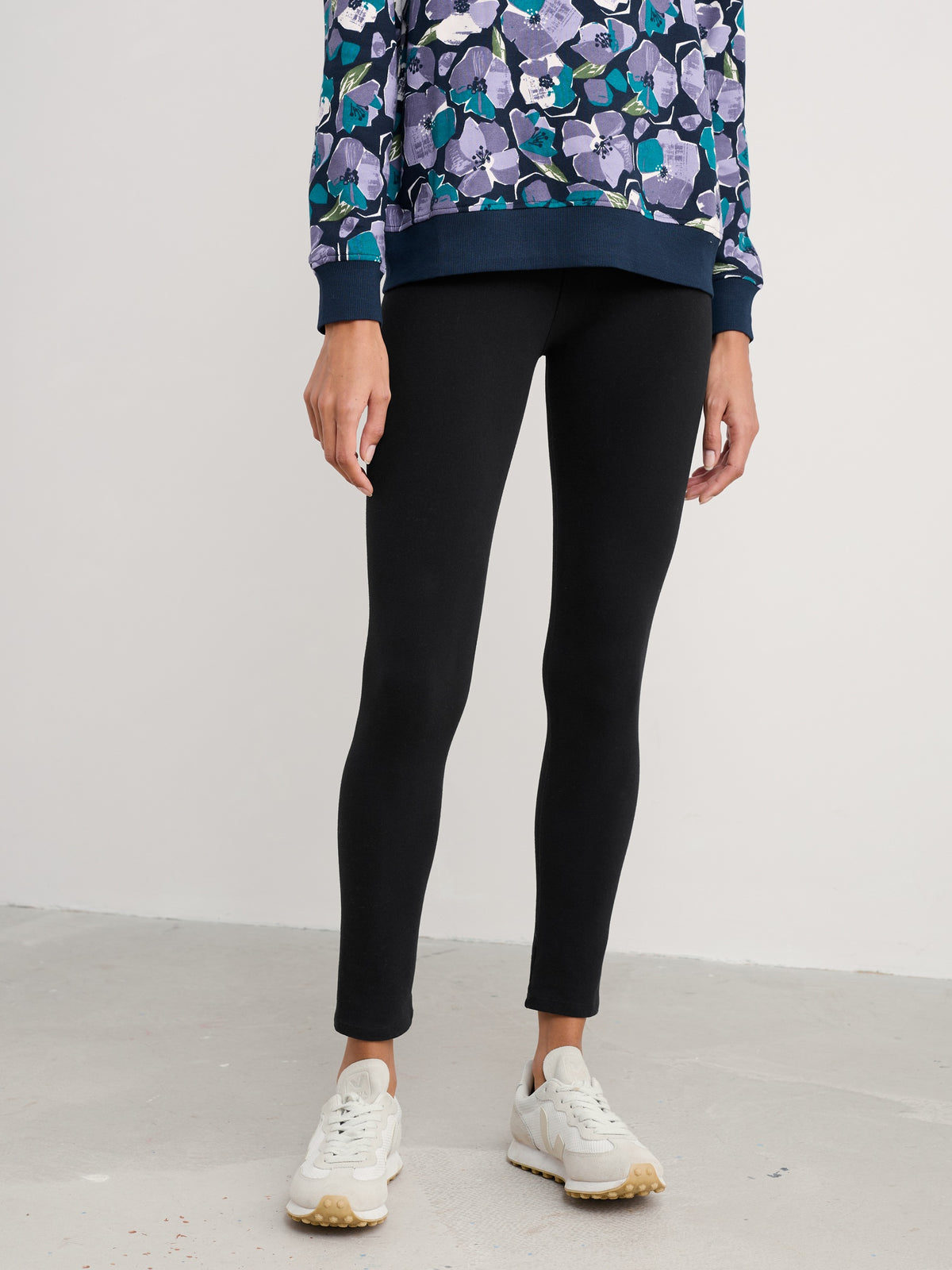 Woman standing wearing black Seasalt Cornwall organic cotton leggings paired with white sneakers.