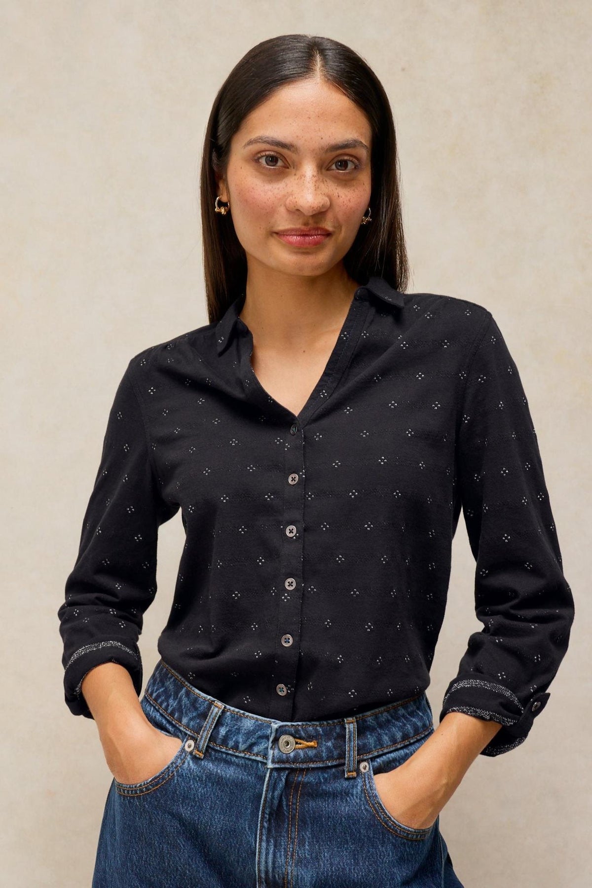 A woman posing in a black button-down cotton shirt with subtle sparkle detail.