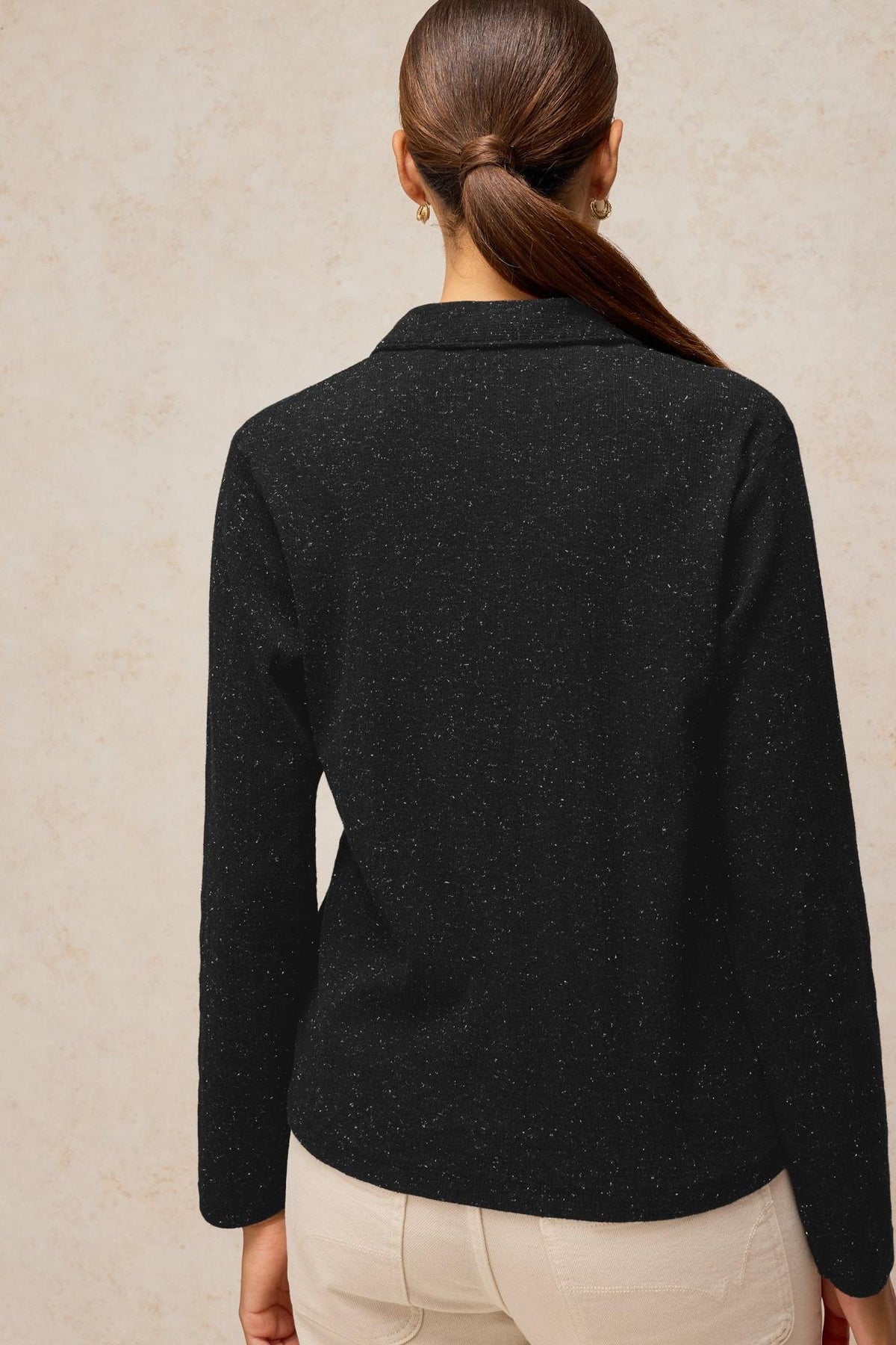 A woman from behind wearing a black long-sleeve sparkle polo top with a collared neckline.