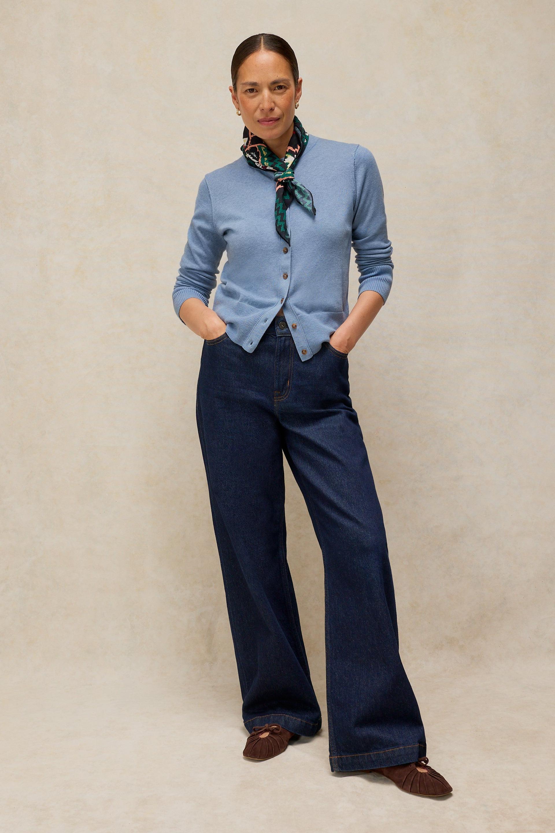 Woman wearing a light blue White Stuff organic cotton cardigan with dark denim wide-leg jeans and a patterned neck scarf