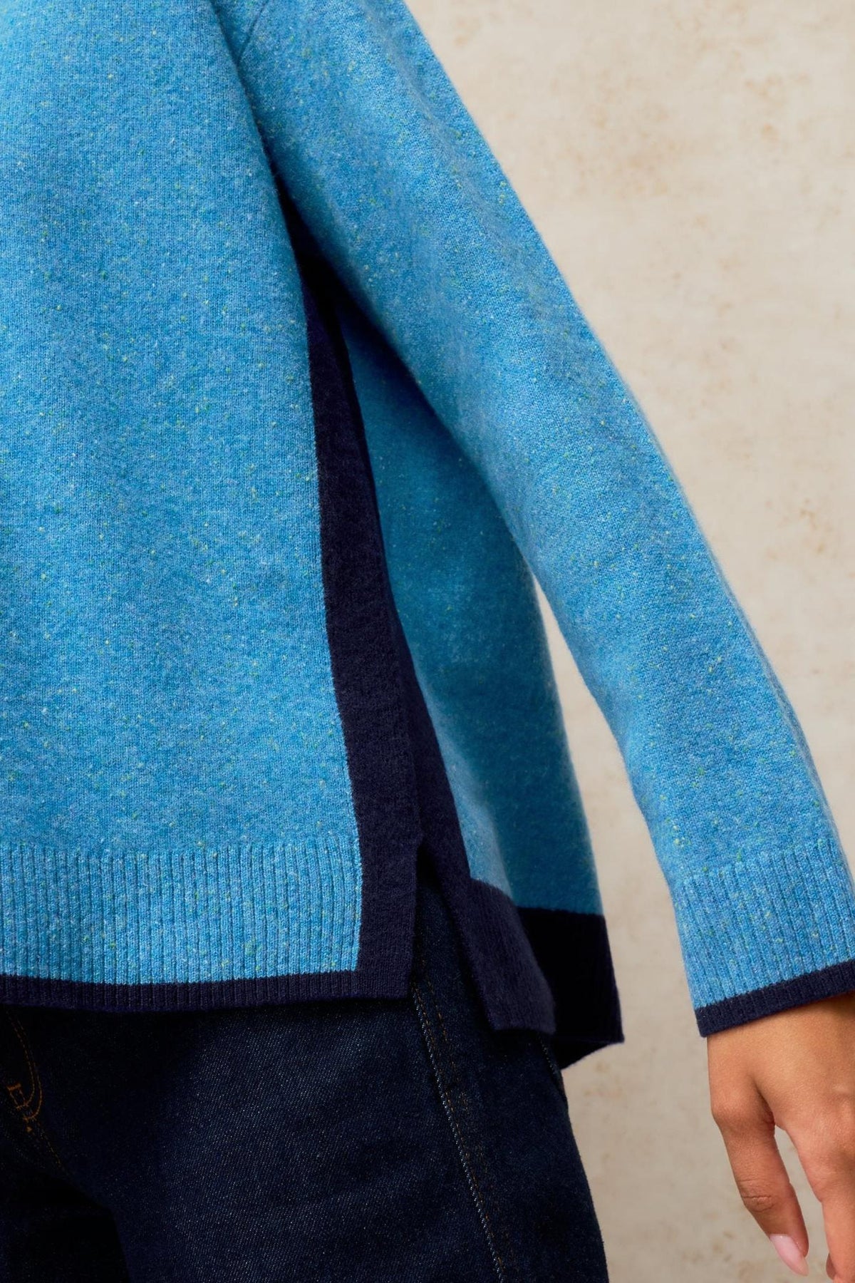 Close-up of a person wearing a textured blue knit cashmere jumper with dark navy side panel detailing.