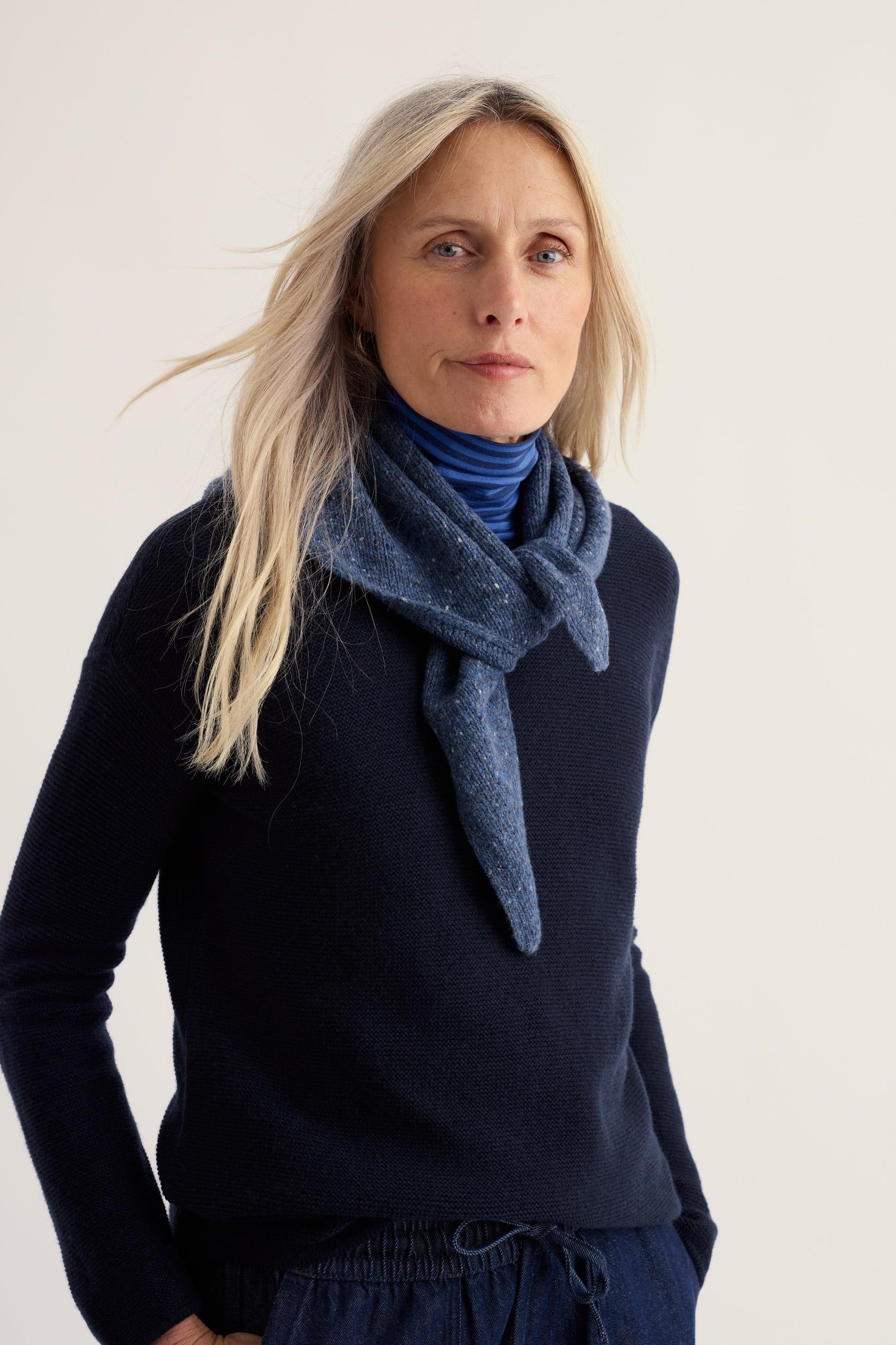 A woman wearing a blue knit scarf and navy sweater against a neutral background.
