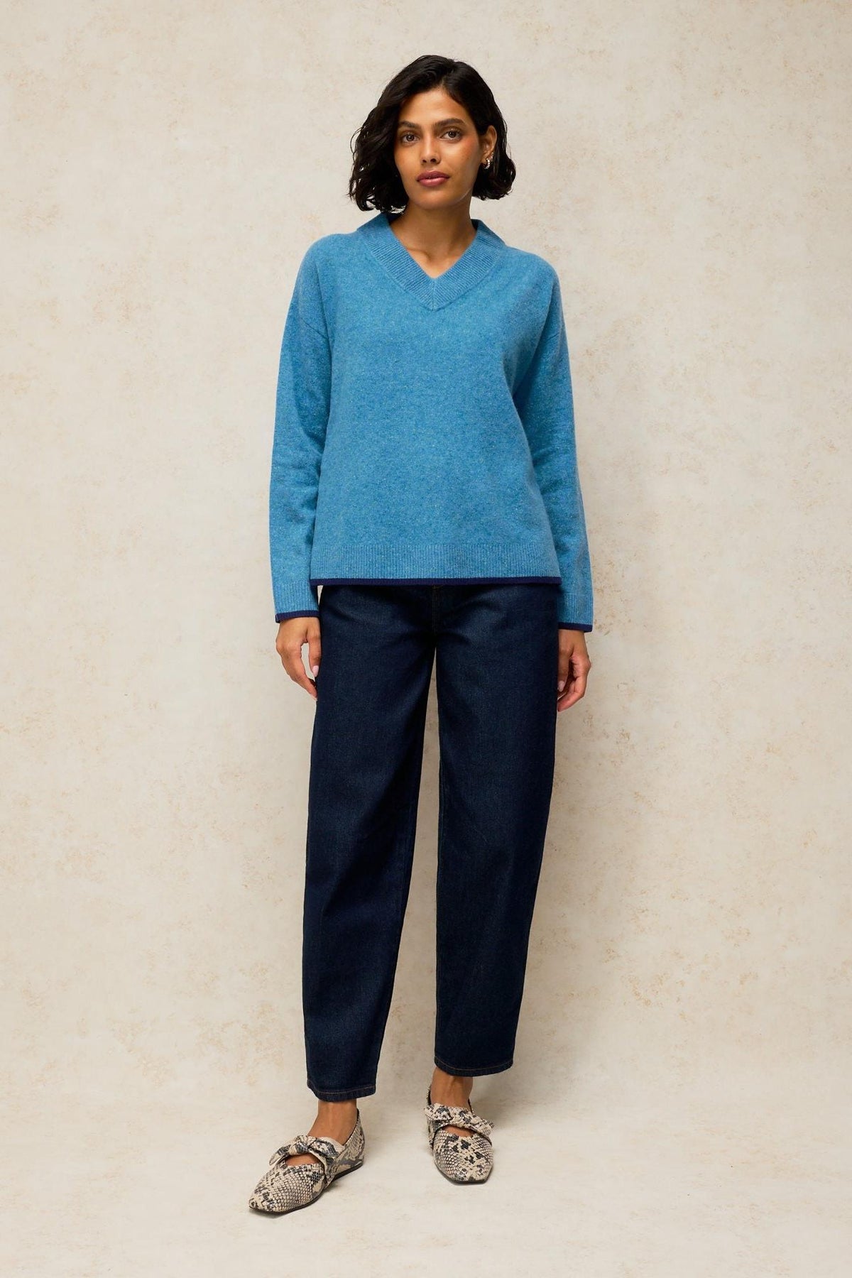 A woman modelling a soft blue knit sweater with a V-neck, paired with dark blue denim jeans.