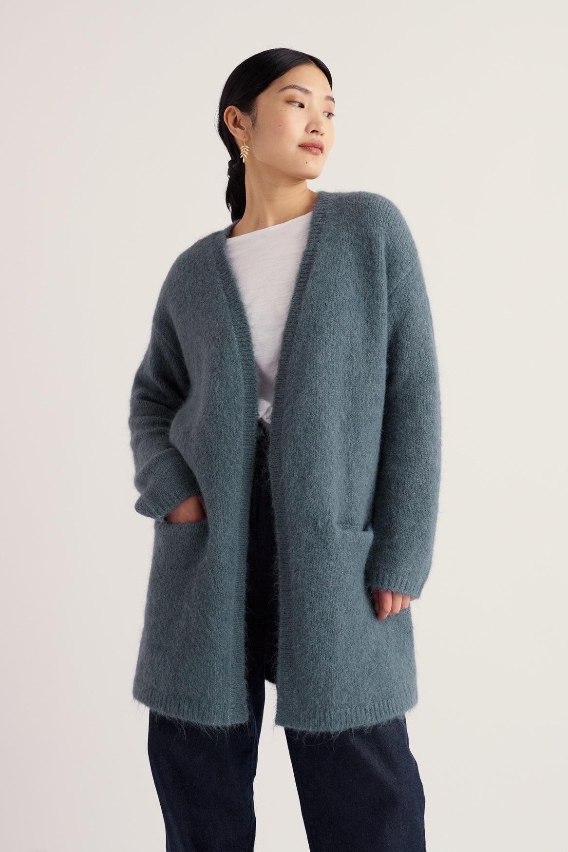 A woman wearing a soft blue long cardigan by Seasalt Cornwall over a white t-shirt against a plain background.