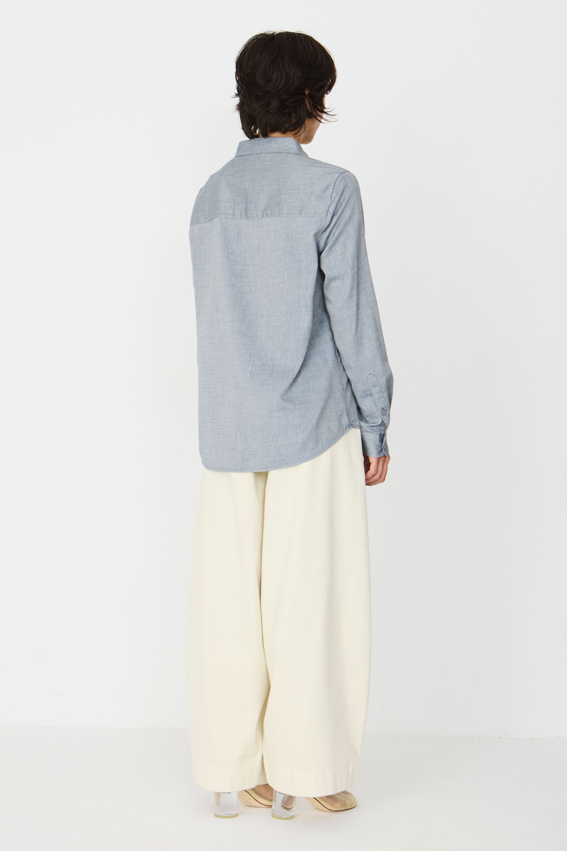 Back view of a woman wearing a blue melange shirt and wide-leg trousers against a white background.