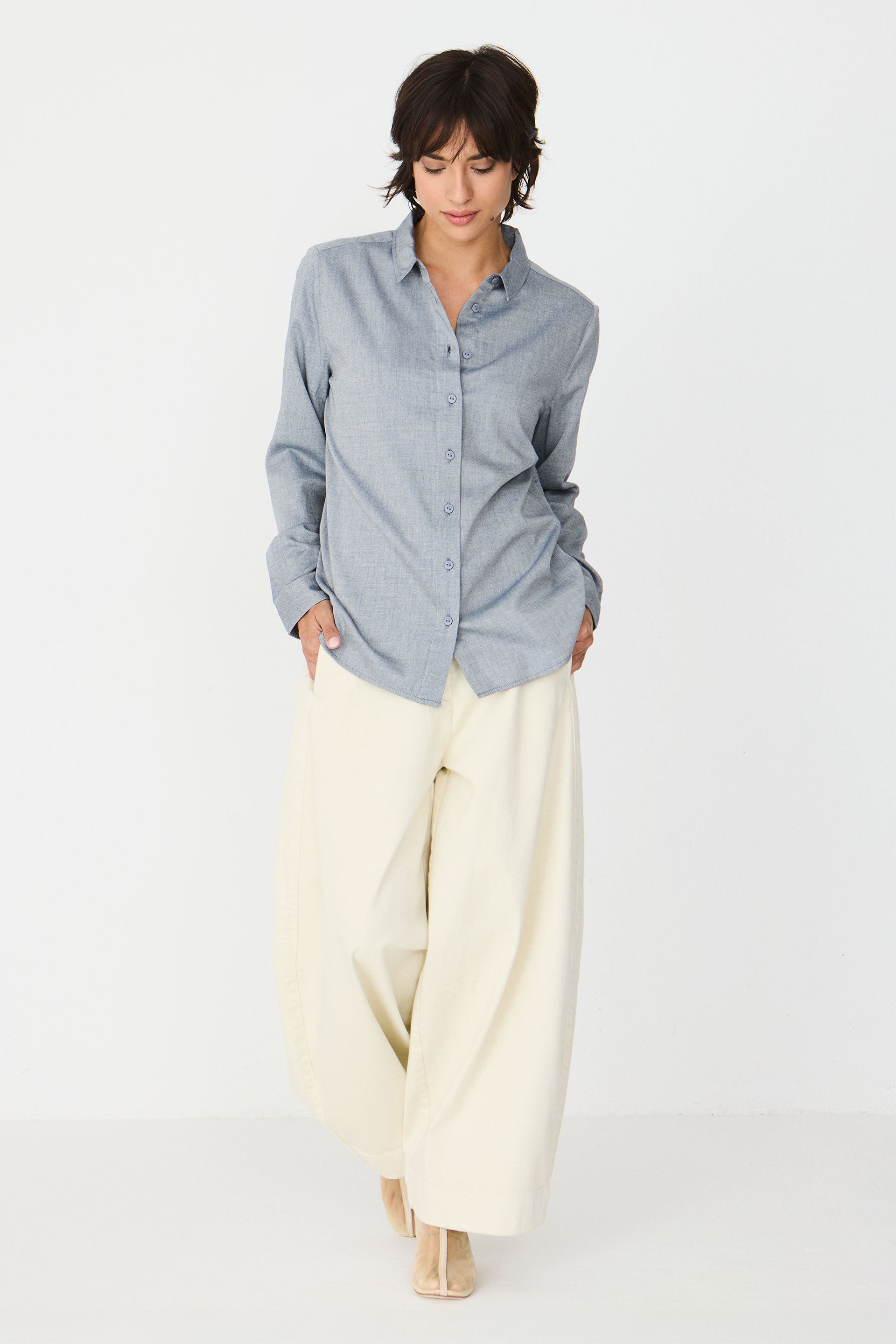 A woman wearing a blue melange button-down shirt paired with cream-colored wide-leg trousers.