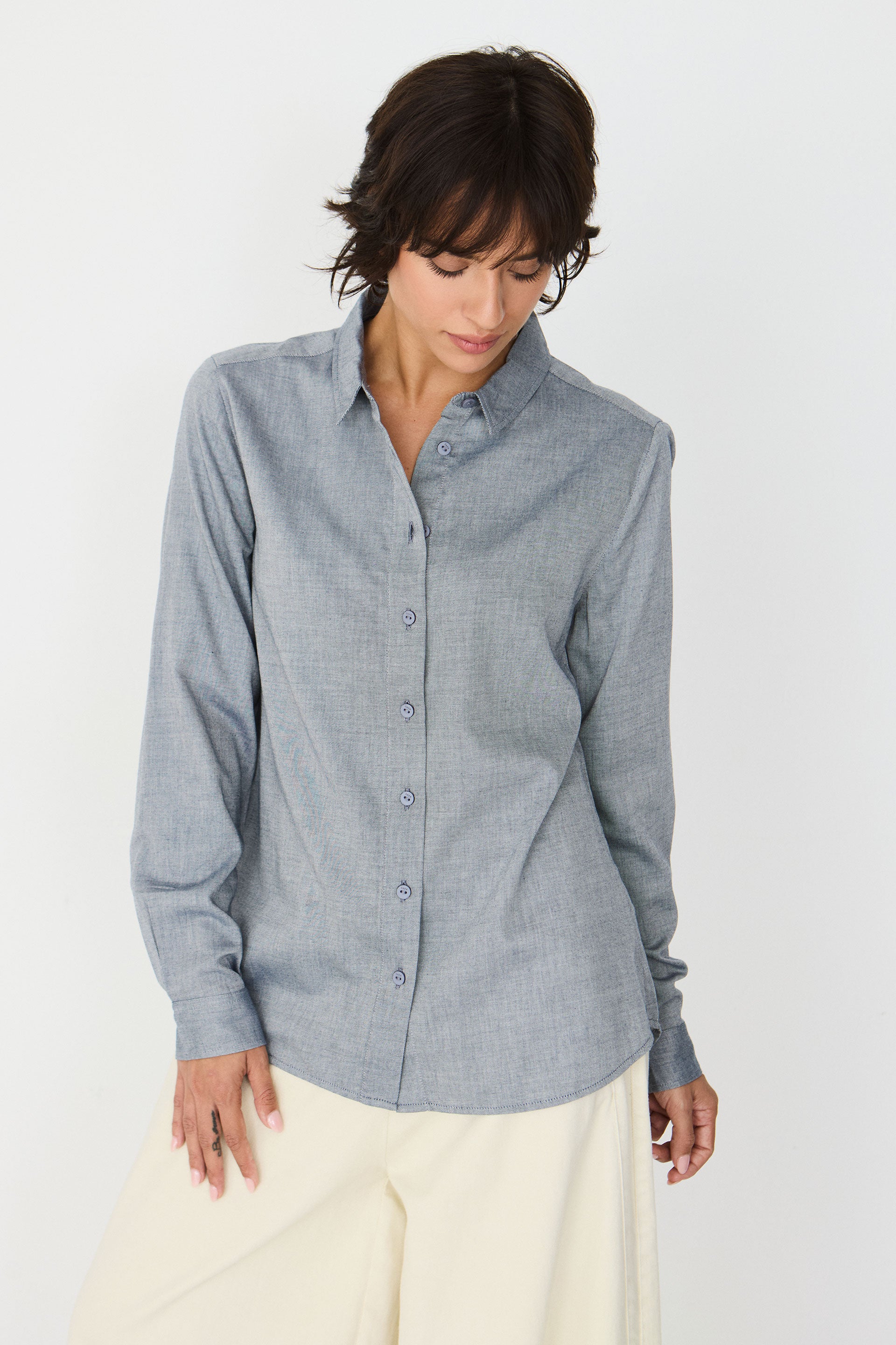 A model wearing a long-sleeved blue melange shirt, styled with cream-colored trousers against a white background.