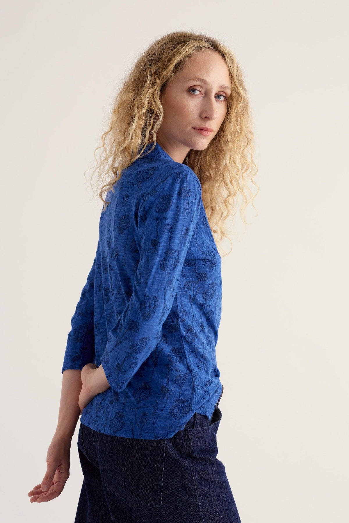 Woman with blonde curly hair wearing a patterned blue organic cotton shirt against a neutral background.