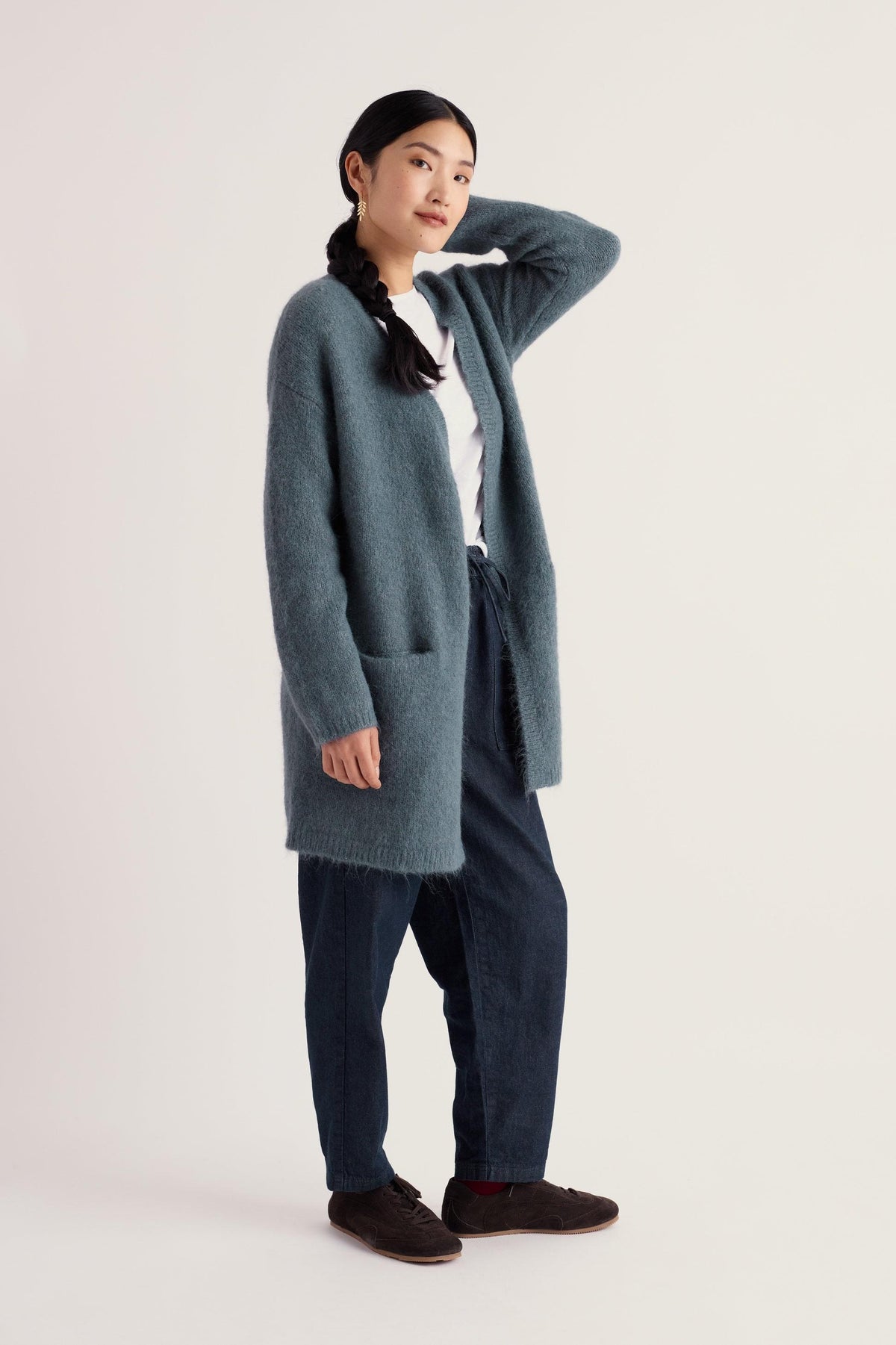 A woman wearing a soft blue Seasalt long cardigan over a white t-shirt and dark jeans against a neutral background.