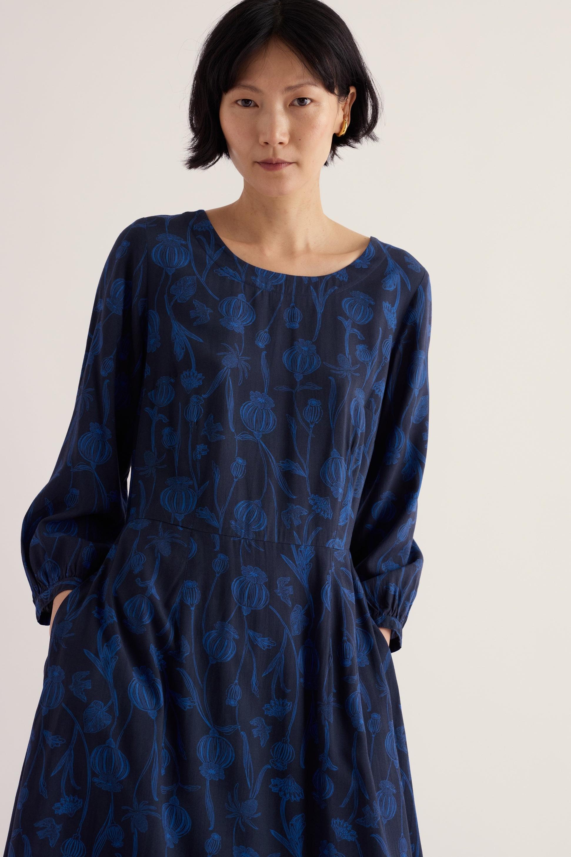 A woman posing in a navy blue Seasalt midi length dress with a botanical floral print.