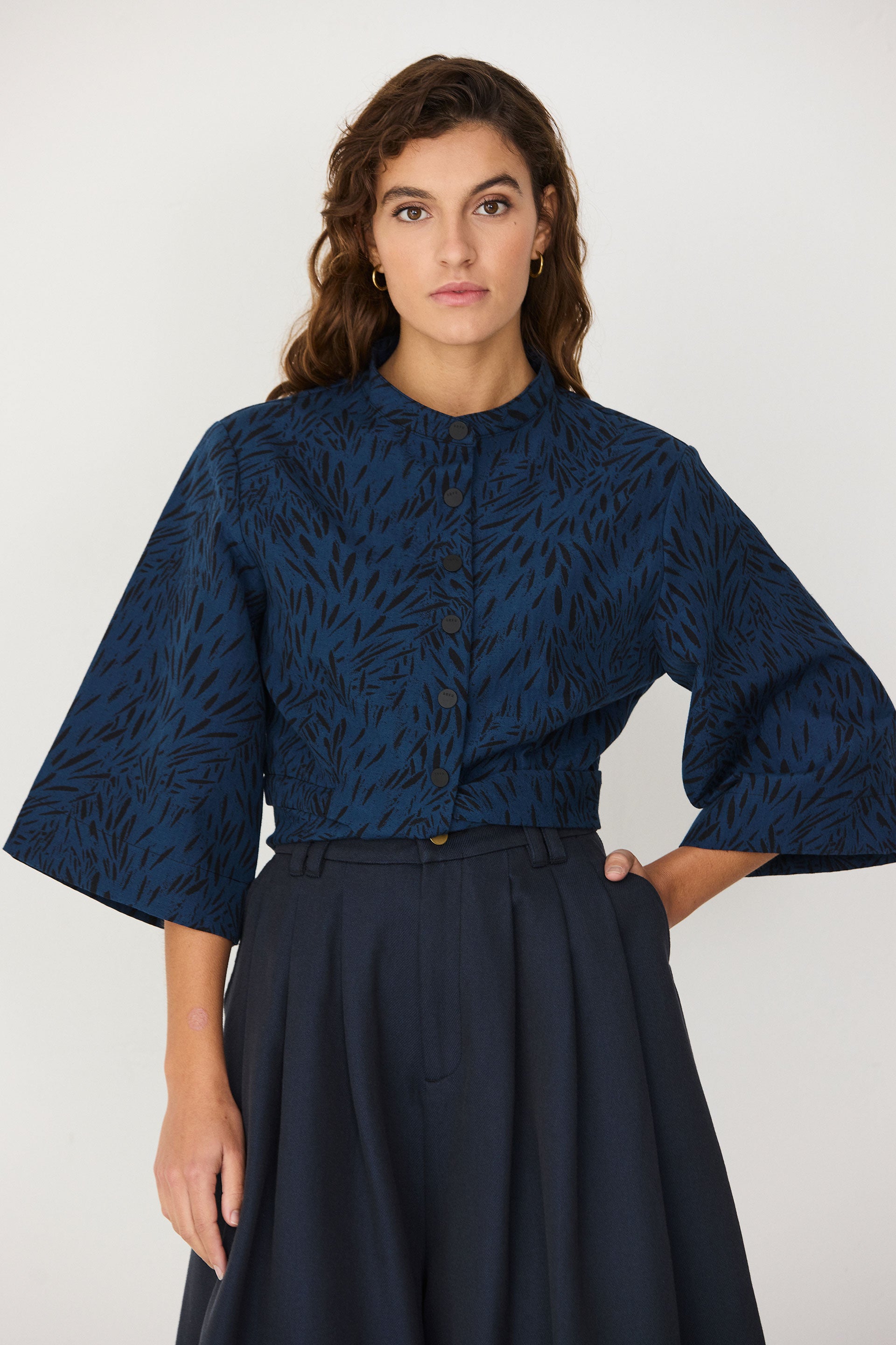 A woman wearing a blue and black patterned SKFK sustainable women's jumpsuit with button-down front.