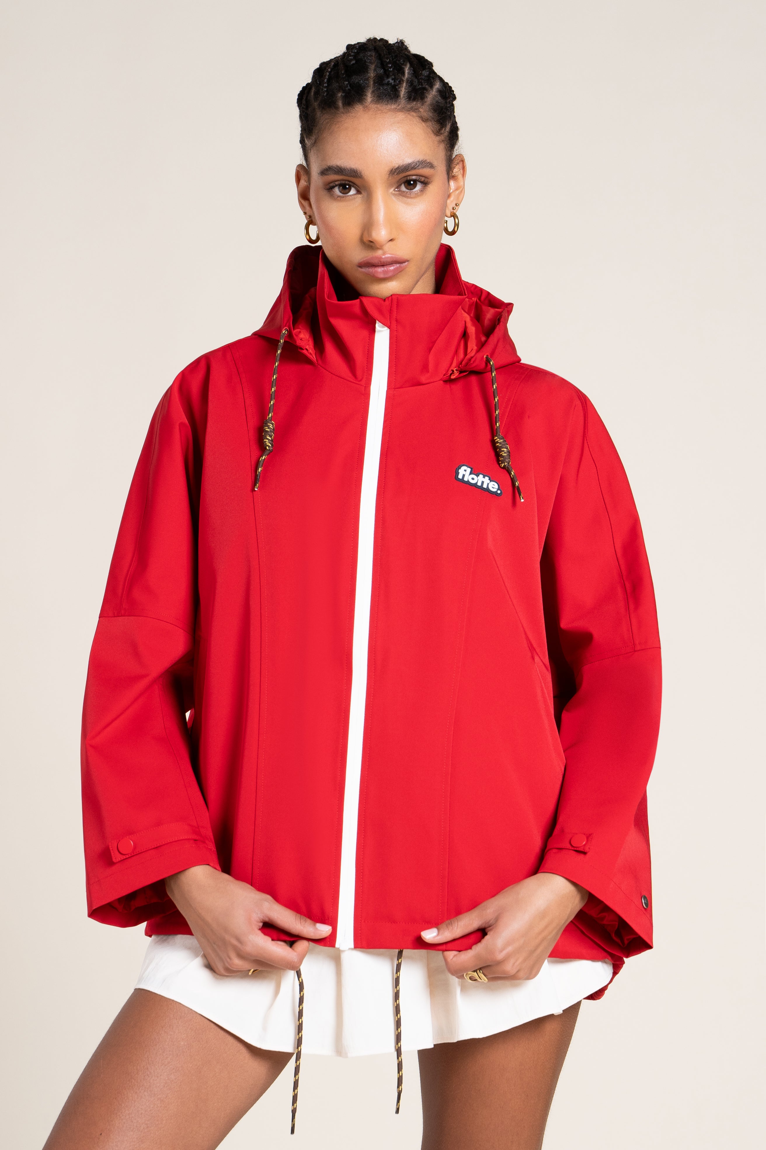 A model wearing a vibrant red Flotte waterproof jacket with a high collar, standing against a neutral studio background.