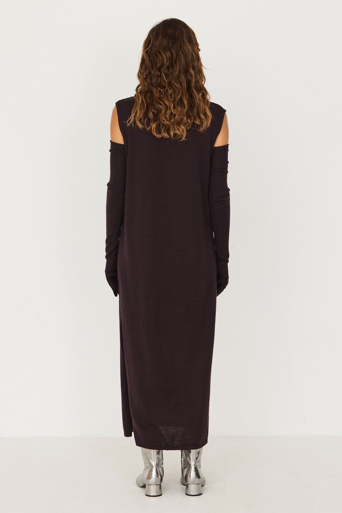 Woman wearing a brown merino wool sleeveless evening dress with detached sleeves against a white background.