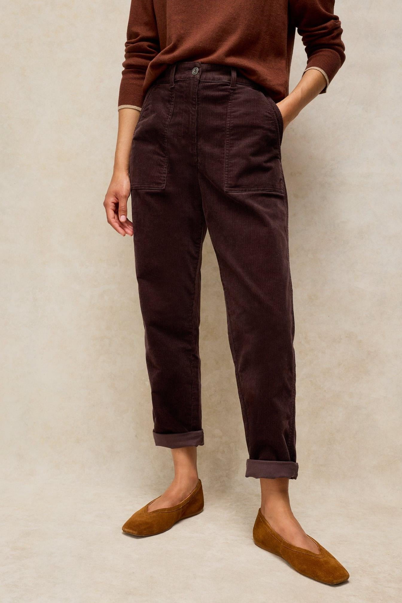 Woman standing wearing dark brown organic cotton corduroy trousers paired with a brown sweater and suede flats.