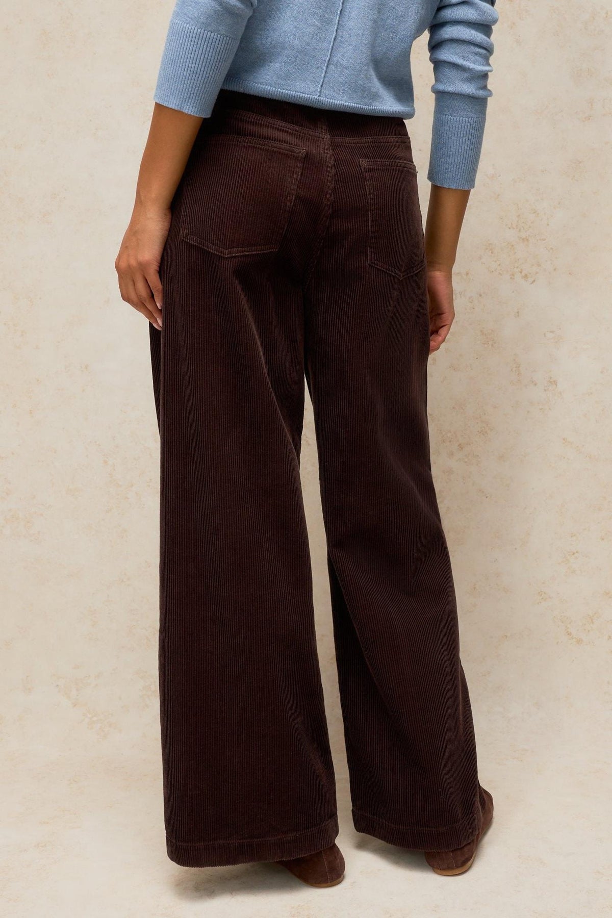 Rear view of a woman wearing wide-leg brown White Stuff cord trousers paired with a light blue sweater.