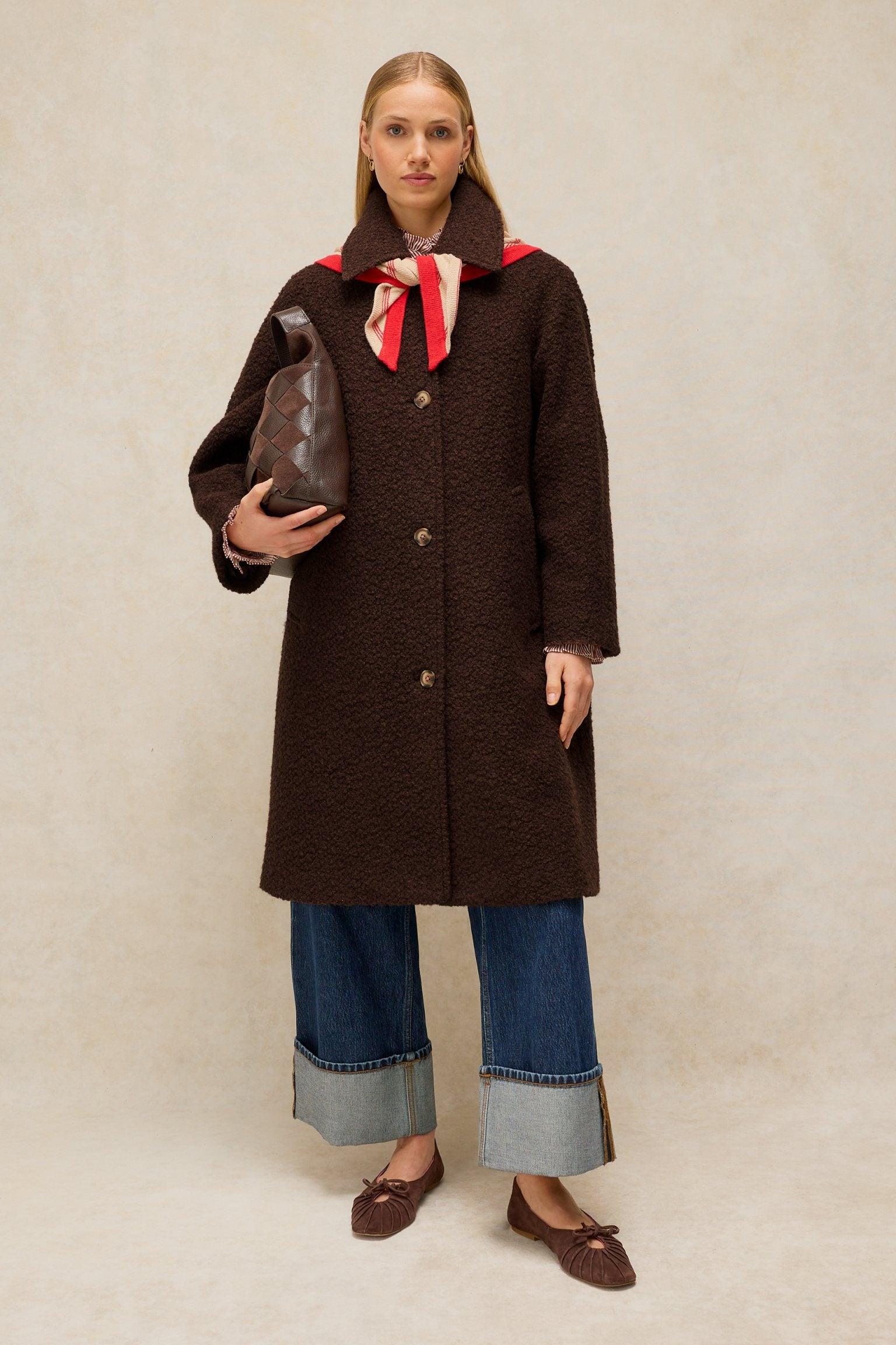 A woman wearing a brown textured White Stuff wool coat, blue cuffed jeans, and holding a brown handbag.