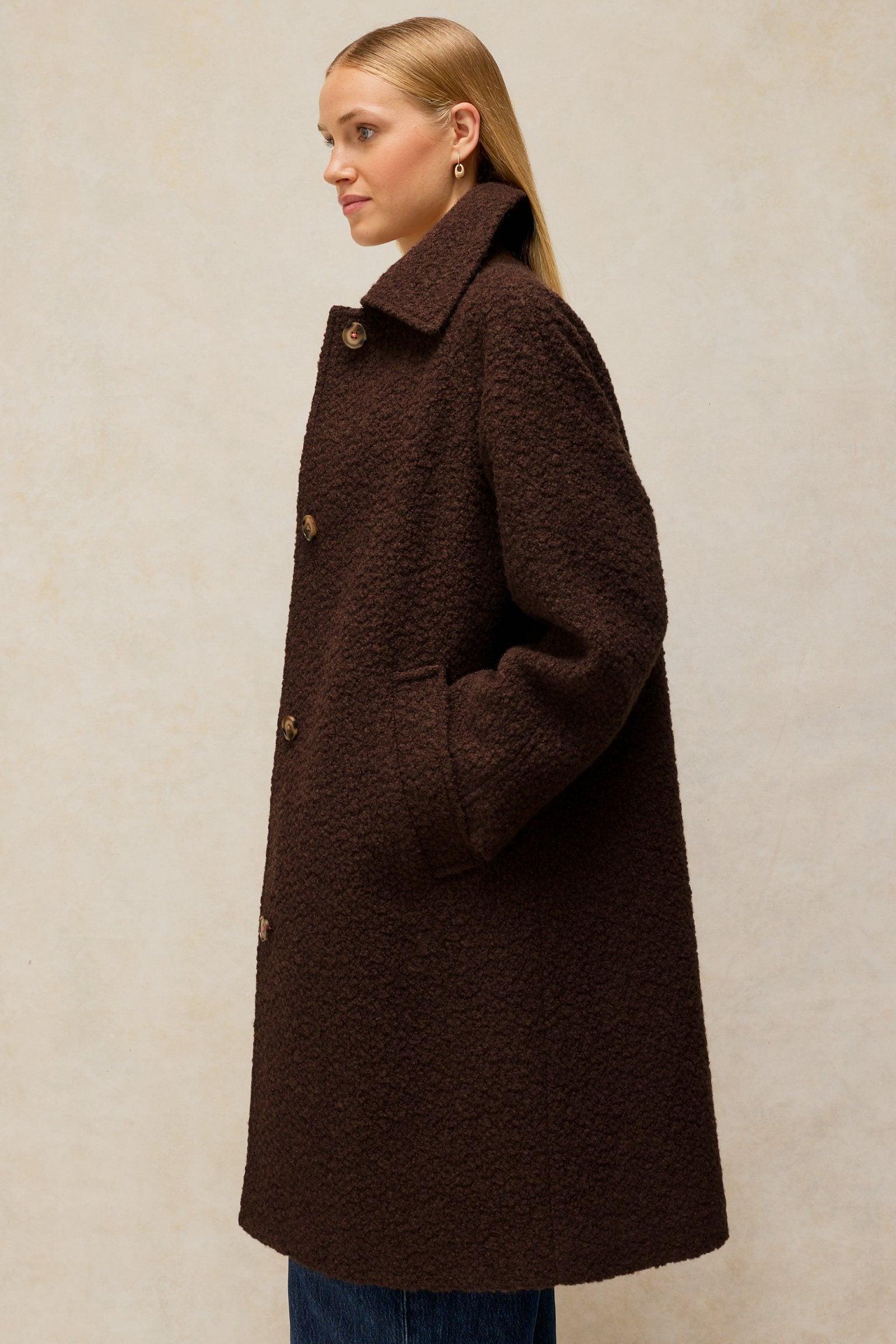 A woman wearing a brown textured wool coat from White Stuff against a neutral background.