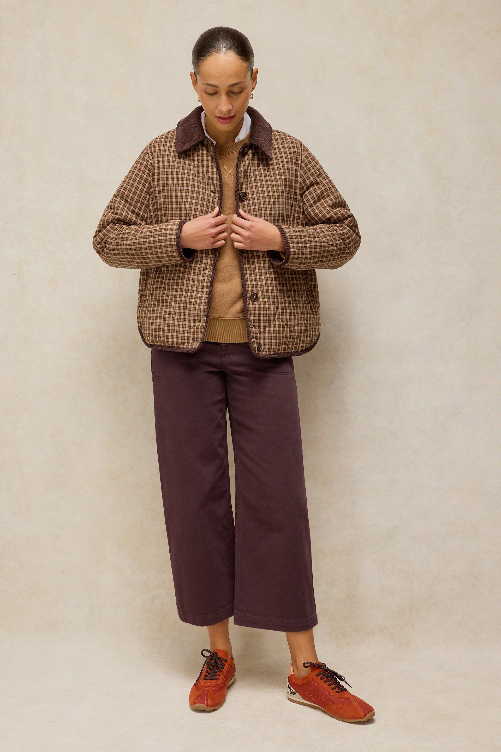 A woman modeling a brown checkered quilted jacket over a tan sweater and dark trousers
