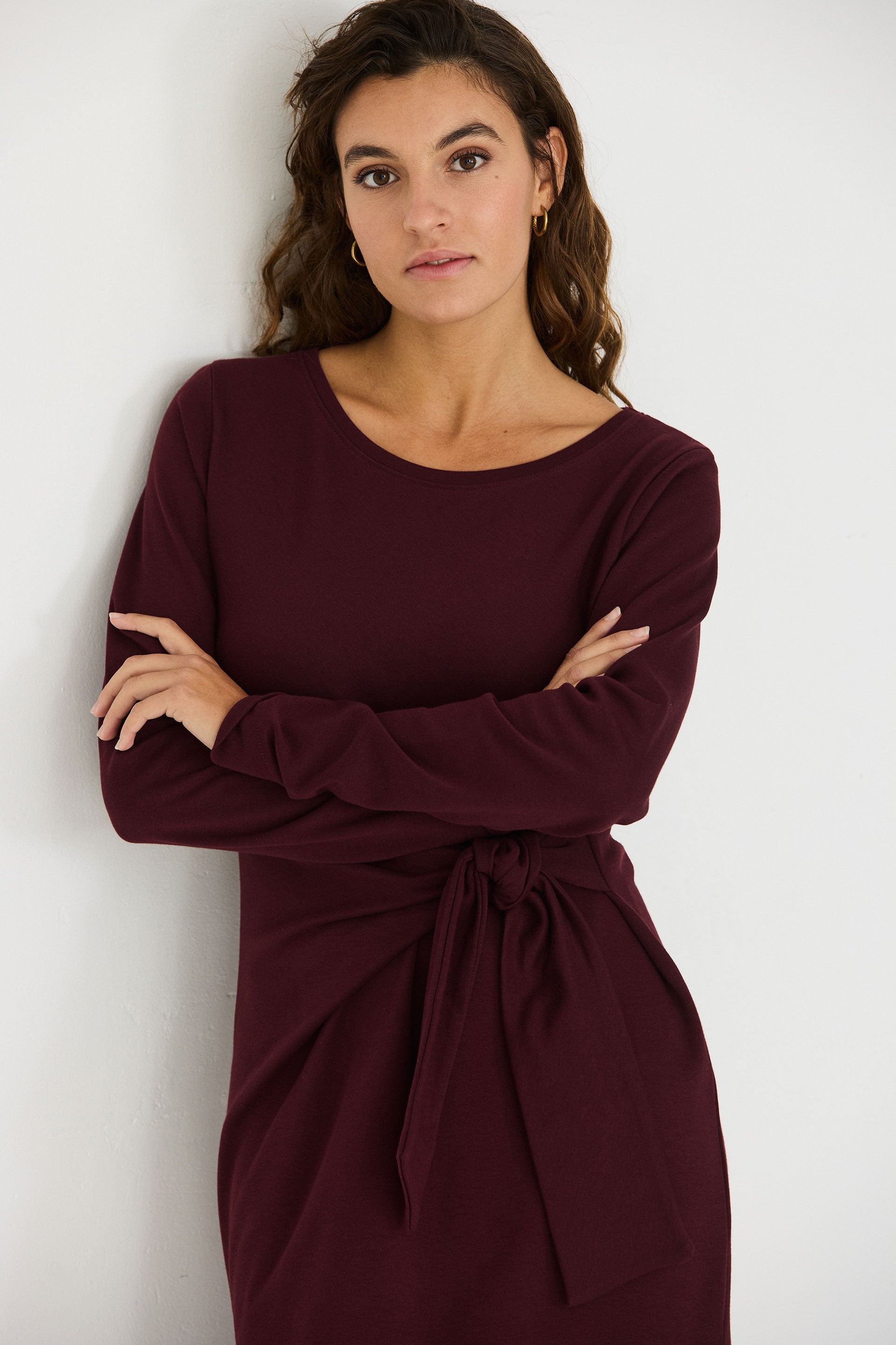 Woman wearing a long-sleeved chocolate brown organic cotton midi dress with a side tie detail.
