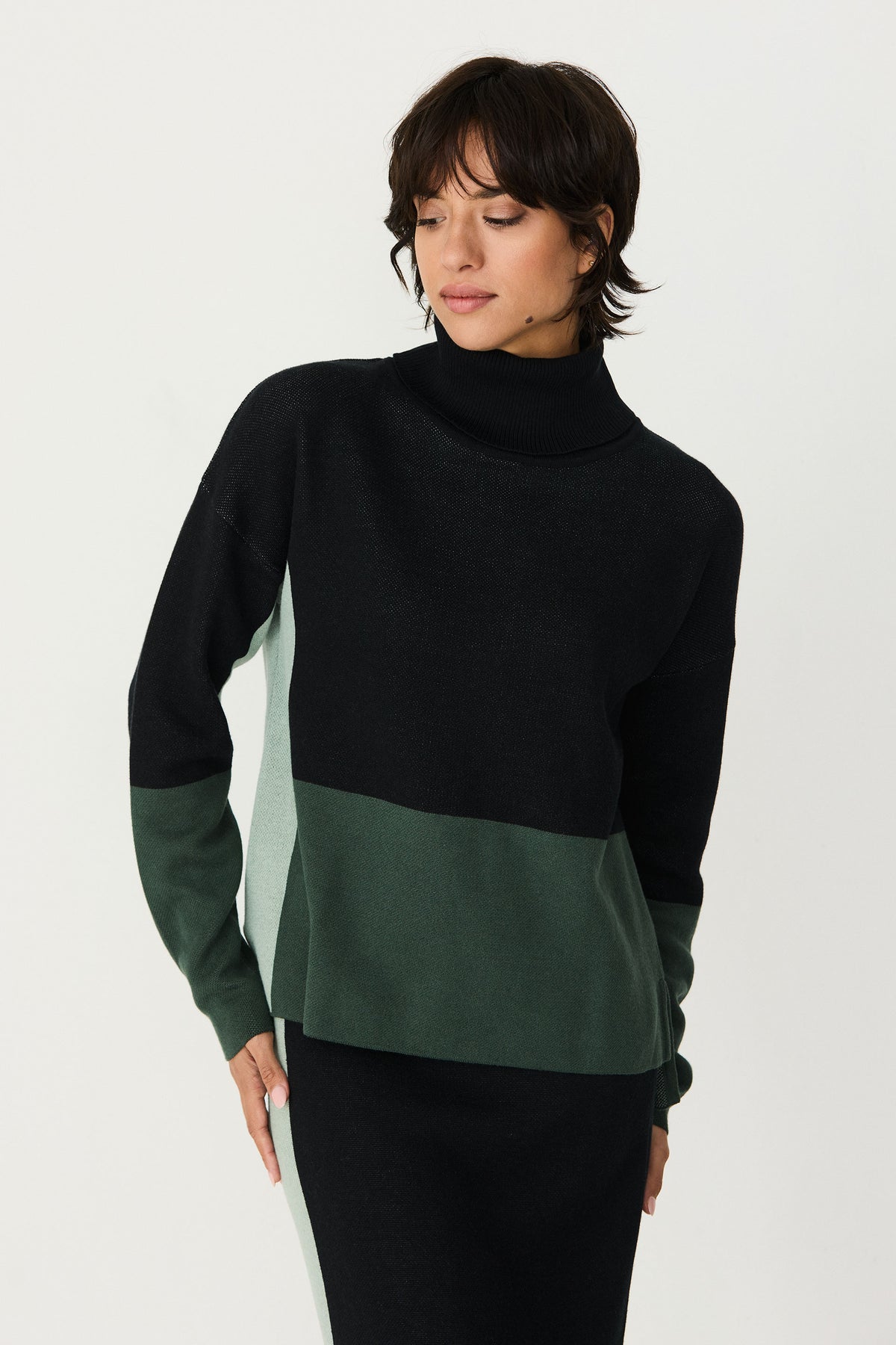 A woman posing in a colourblock cotton sweater with black, dark green, and light green panels.