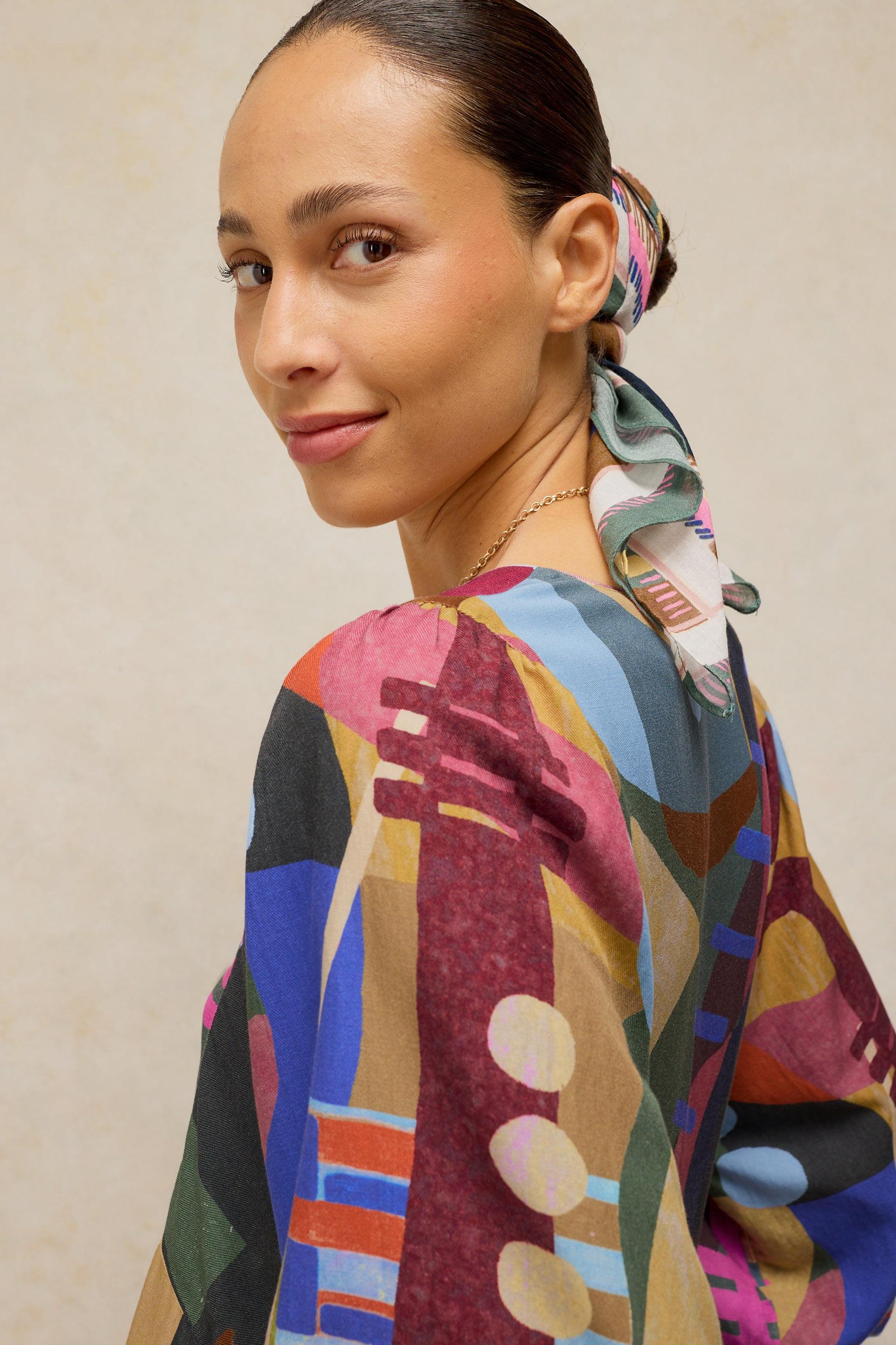 Woman wearing a colorful Ecovero patterned dress and matching head scarf looking over her shoulder.