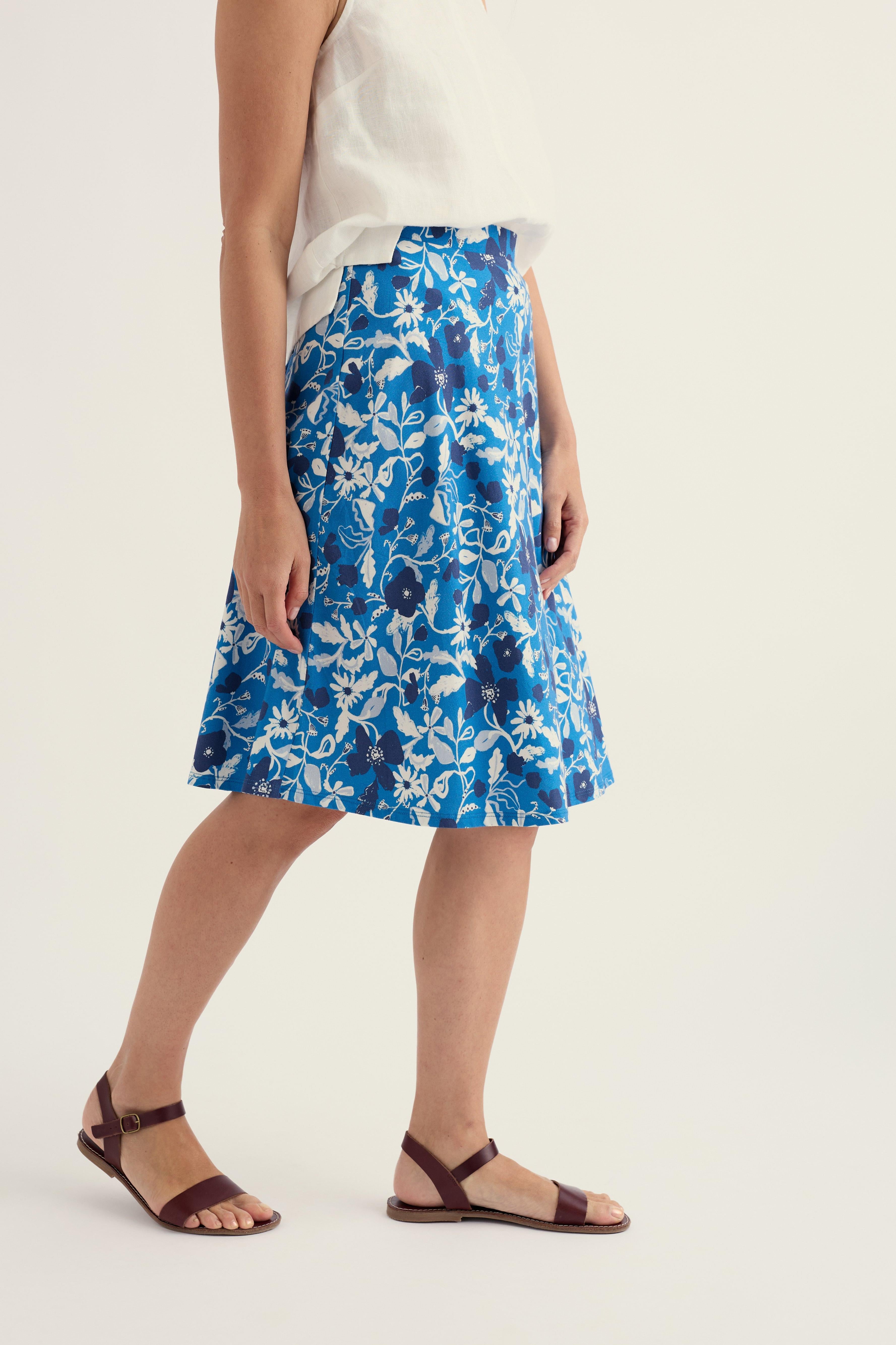 Woman wearing a bright blue floral midi skirt and a sleeveless white top against a white background.