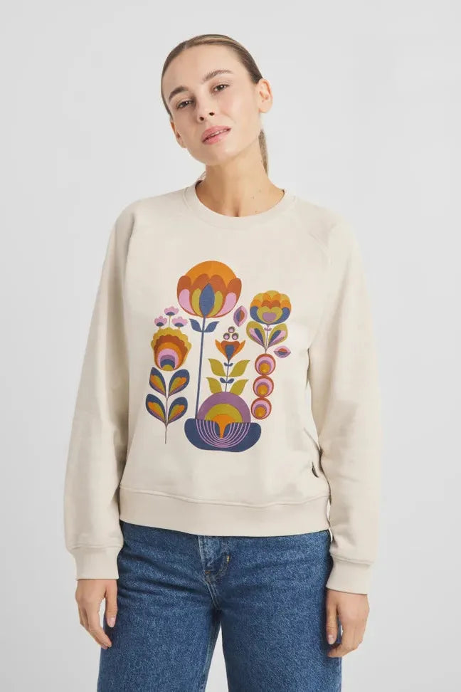 A woman posing in a beige cotton sweatshirt featuring a colourful floral print design.