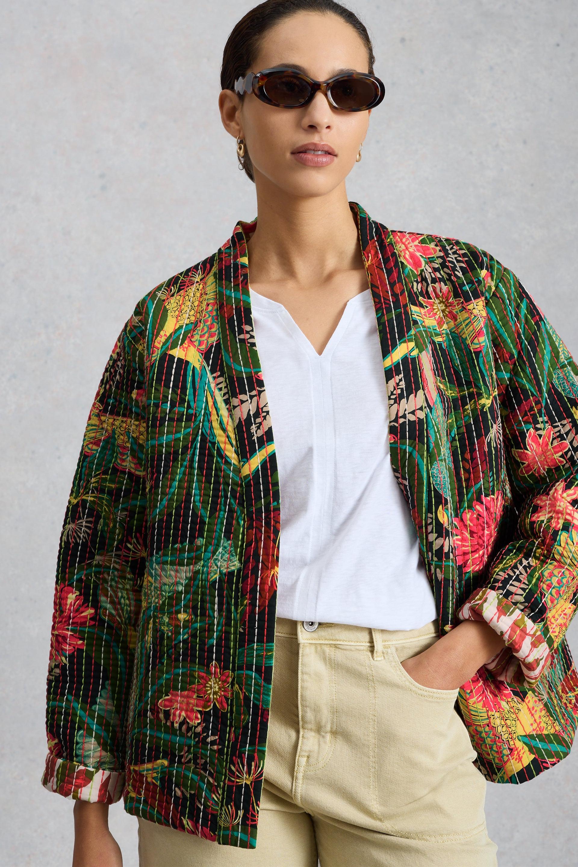 Woman wearing a colourful floral quilted jacket over a white organic cotton top against a neutral background.