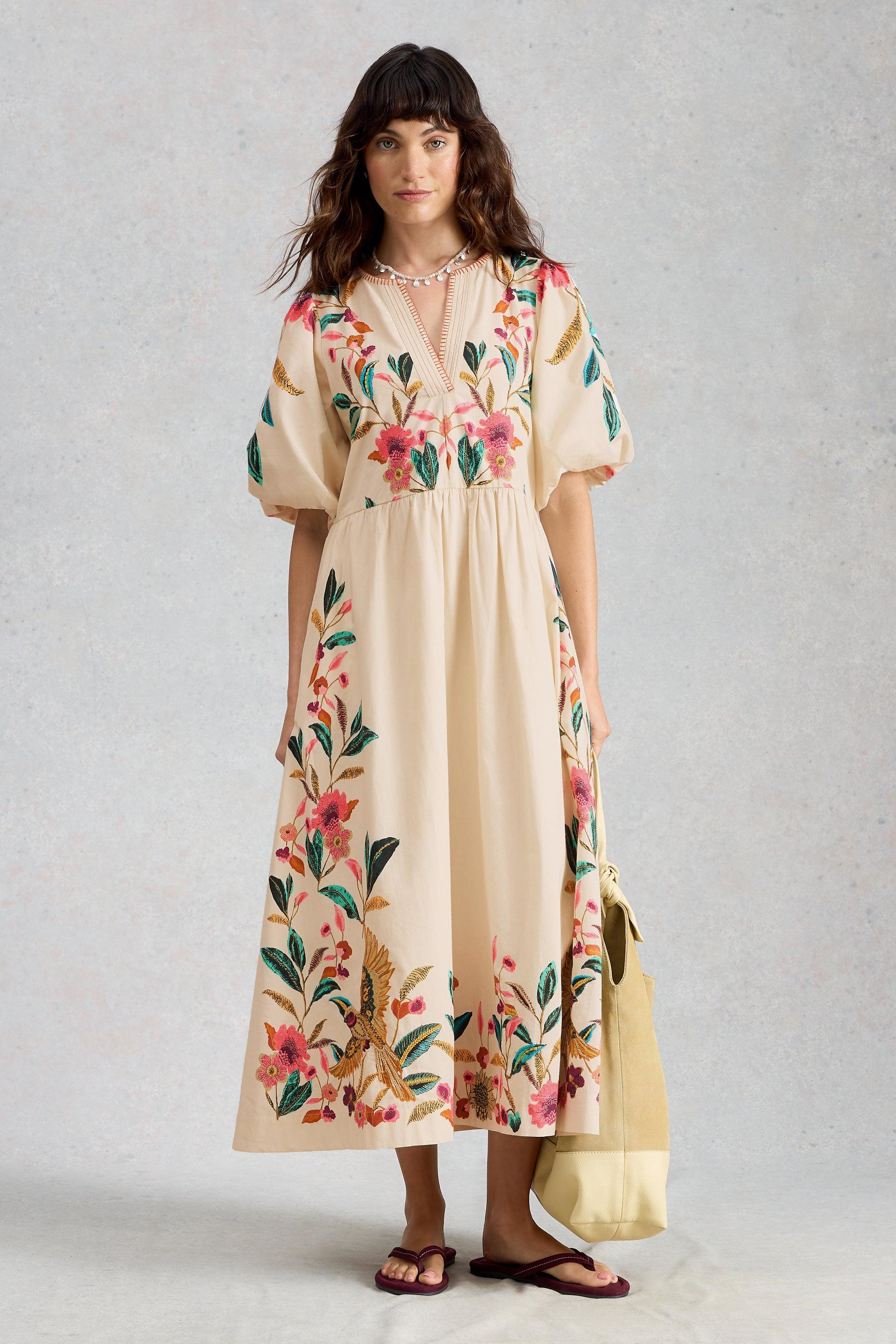 A woman modeling an organic cotton floral midi occasion dress against a light neutral background.