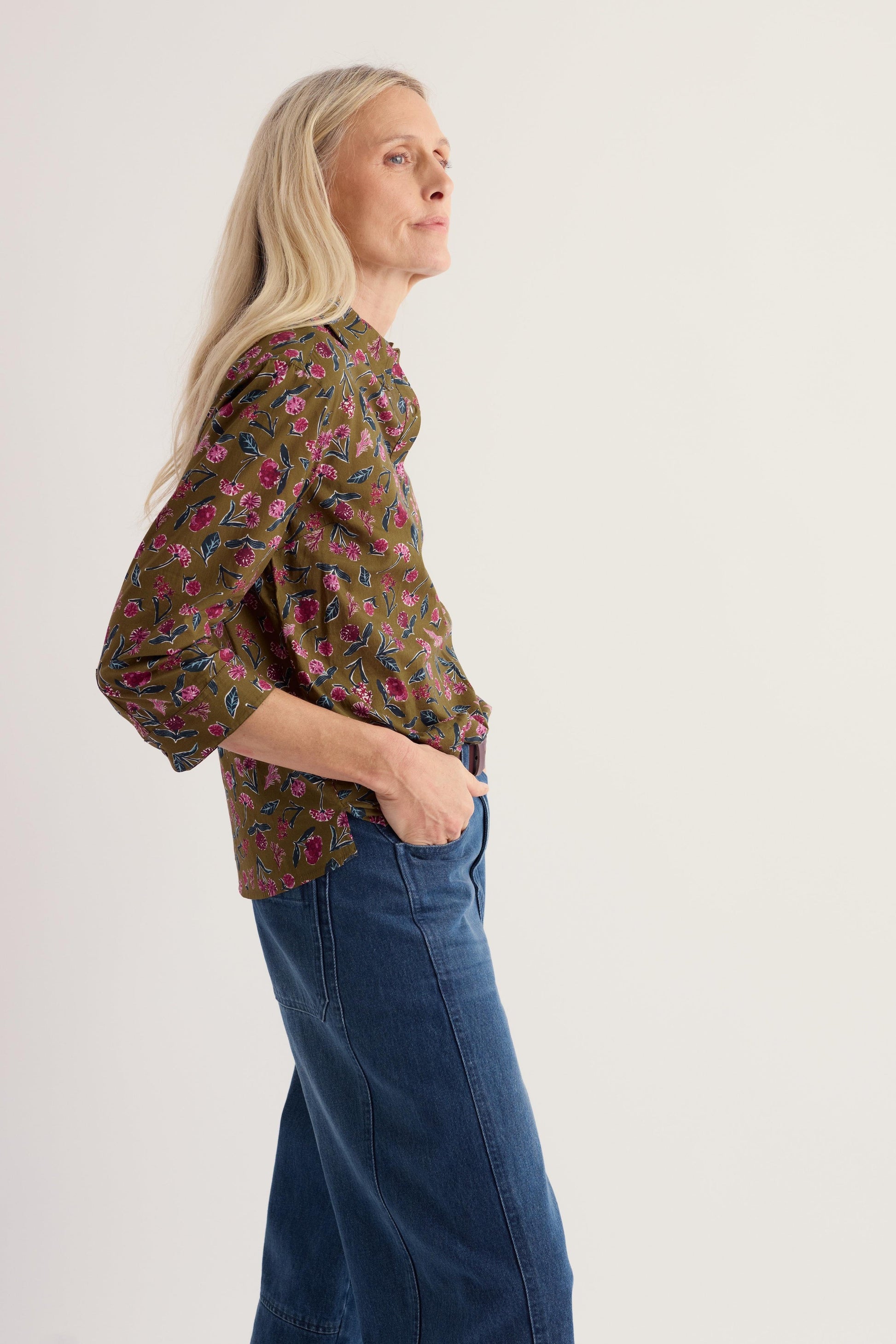 Mature woman modeling a Seasalt floral organic cotton top with blue jeans against a plain white background.