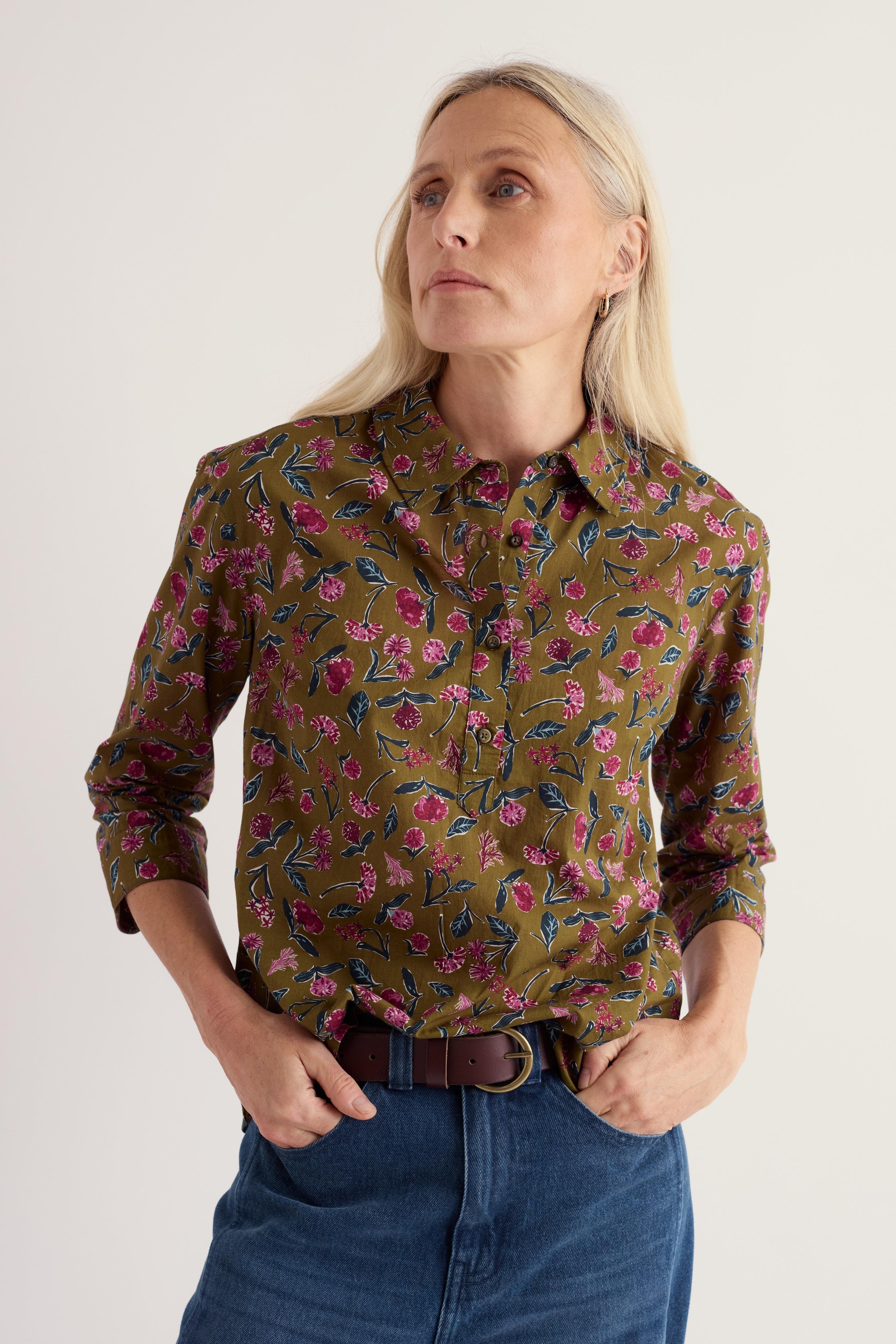 A woman wearing a long-sleeved olive floral print organic cotton top with a button-down collar and blue jeans.