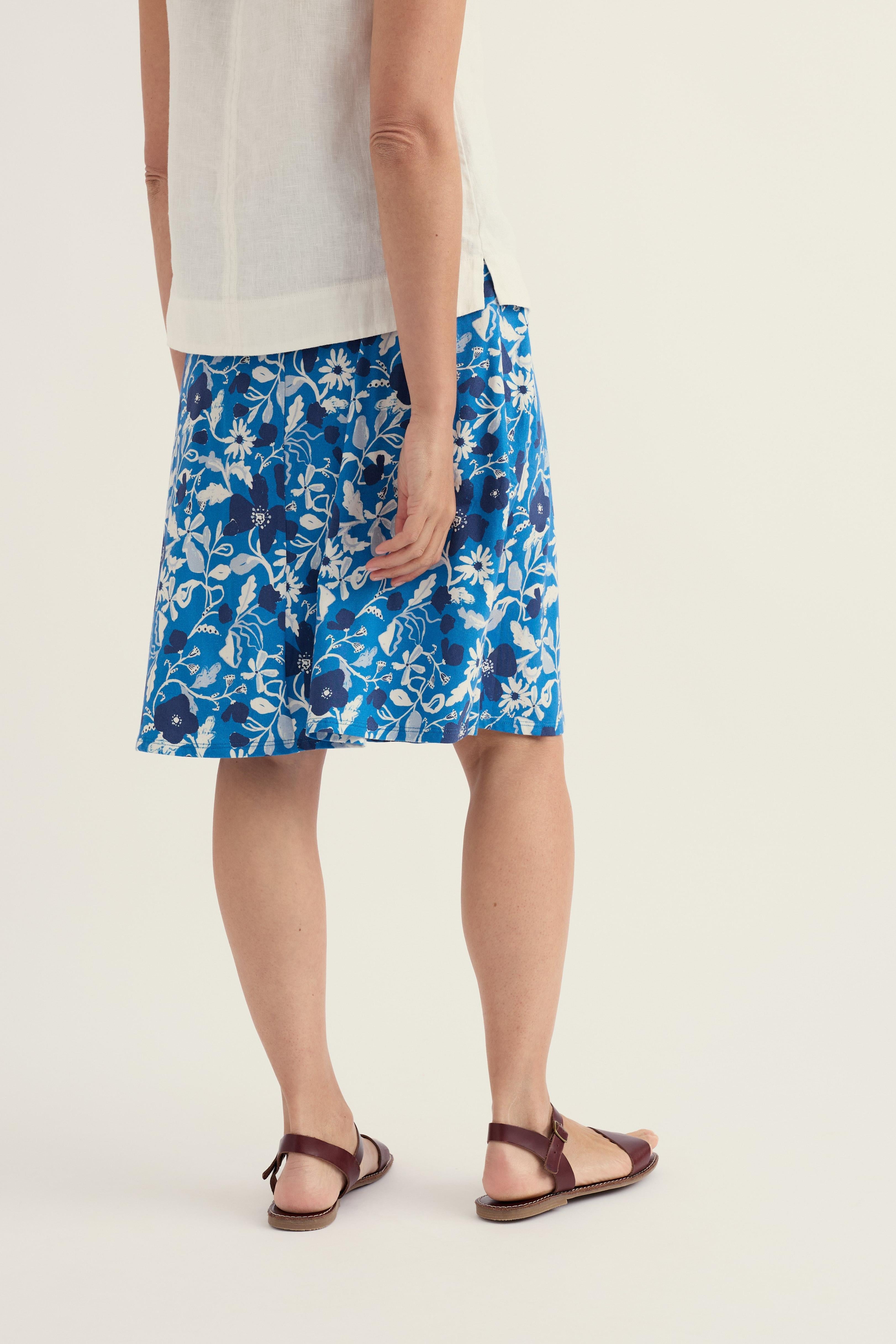Woman standing from behind wearing a blue floral A-line skirt and a simple white sleeveless top against a white background.