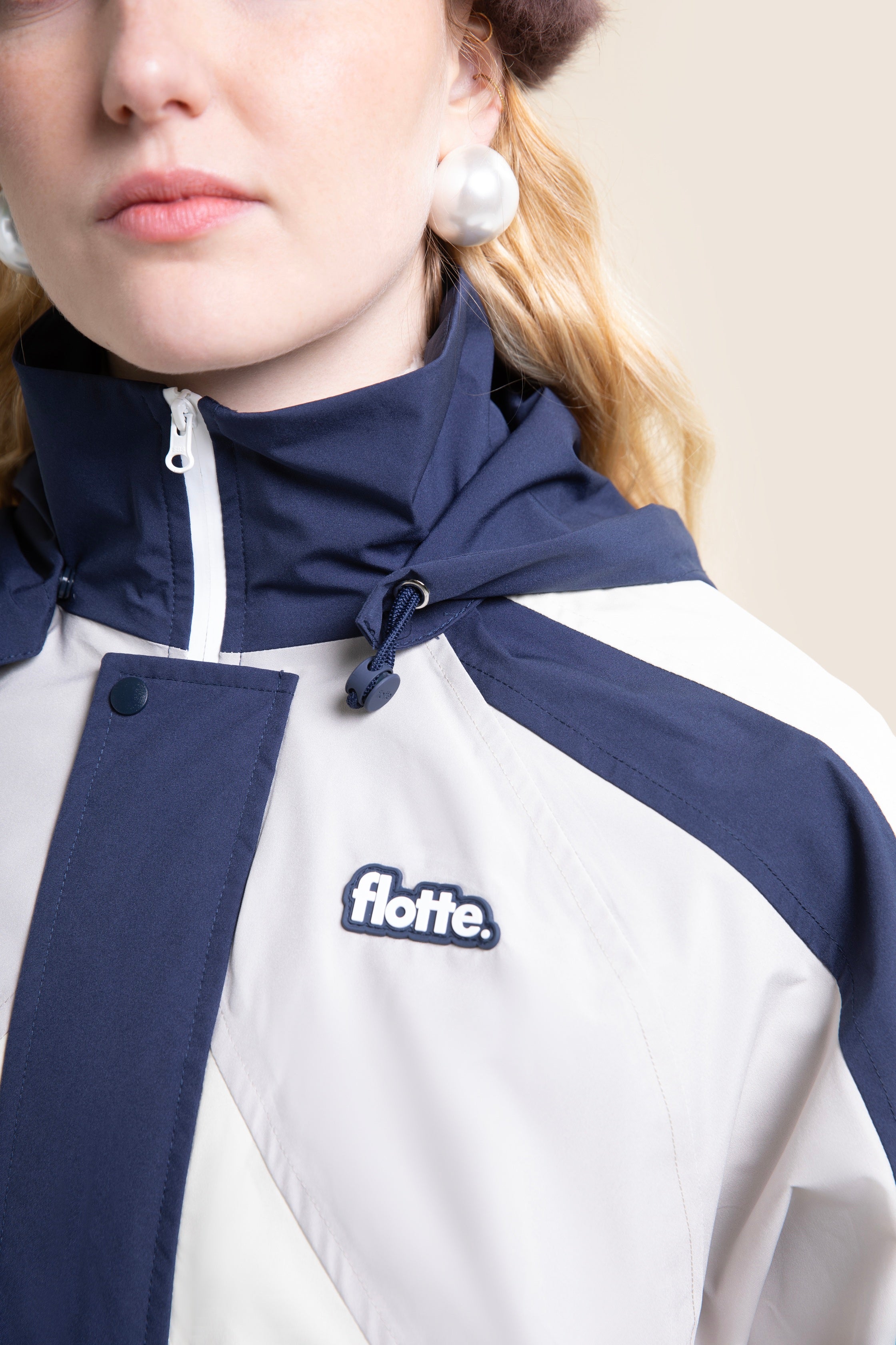 A woman wearing a stylish, navy and white waterproof jacket from Flotte, featuring a hood and recycled polyester fabric.