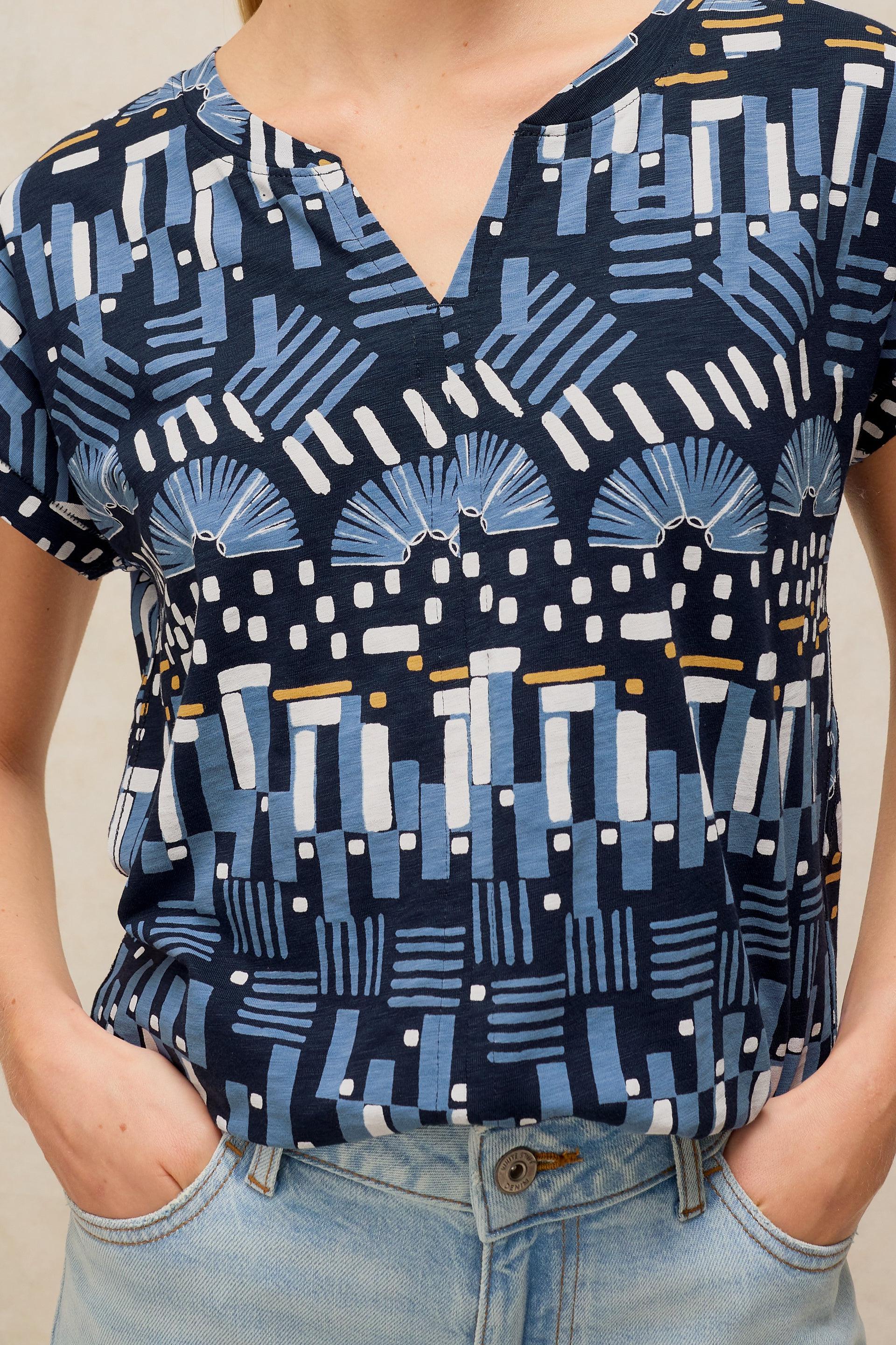 A person wearing a short-sleeved cotton top with a blue and white geometric pattern and light wash jeans