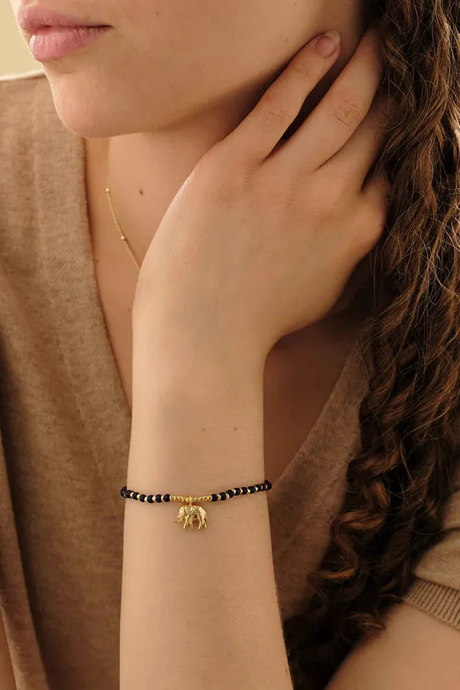 Woman wearing a gold bracelet with black beads on her wrist.
