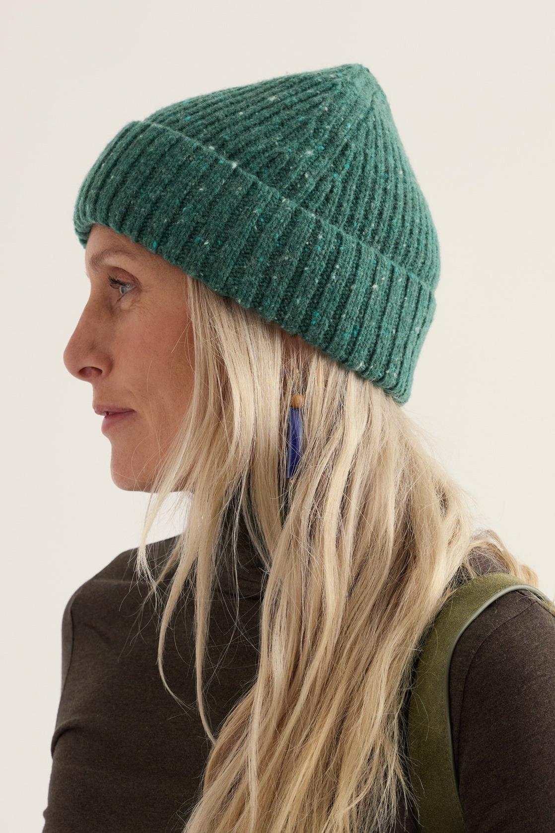 A woman wearing a textured green merino wool hat against a neutral background.