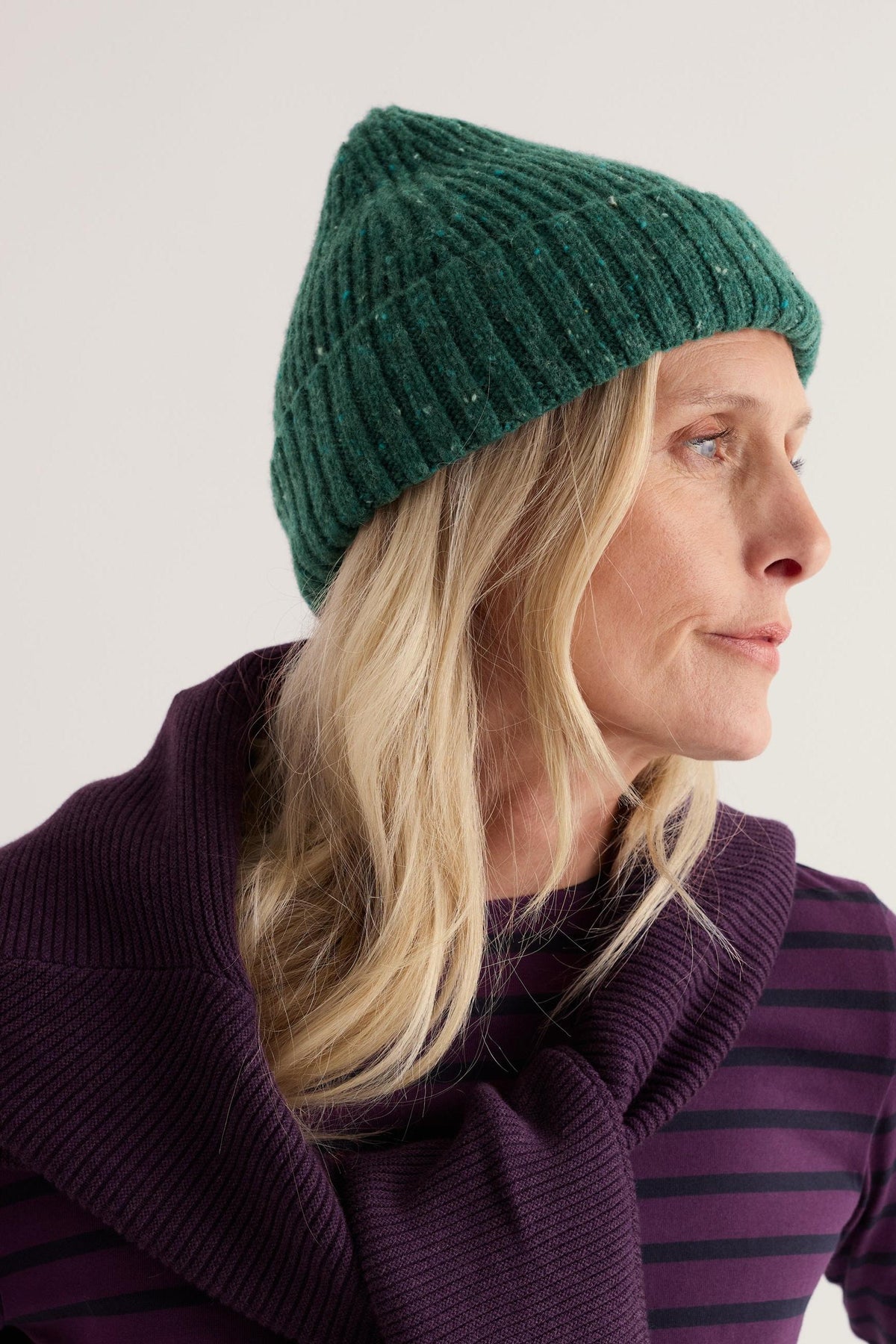 A woman wearing a textured green merino wool hat looking to the side against a neutral background.