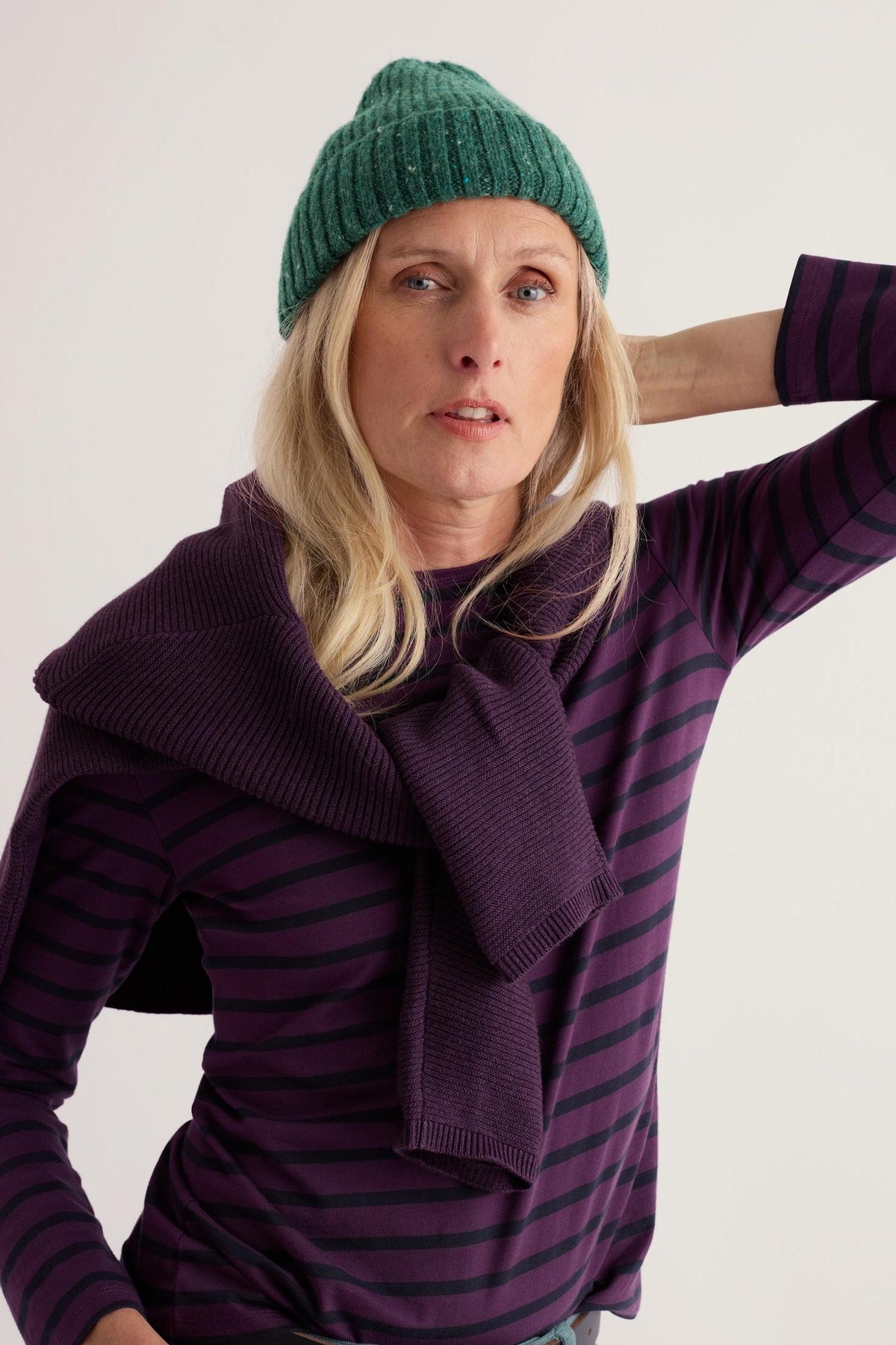 Woman posing in a cozy green merino wool knit hat and a striped purple top against a light background.