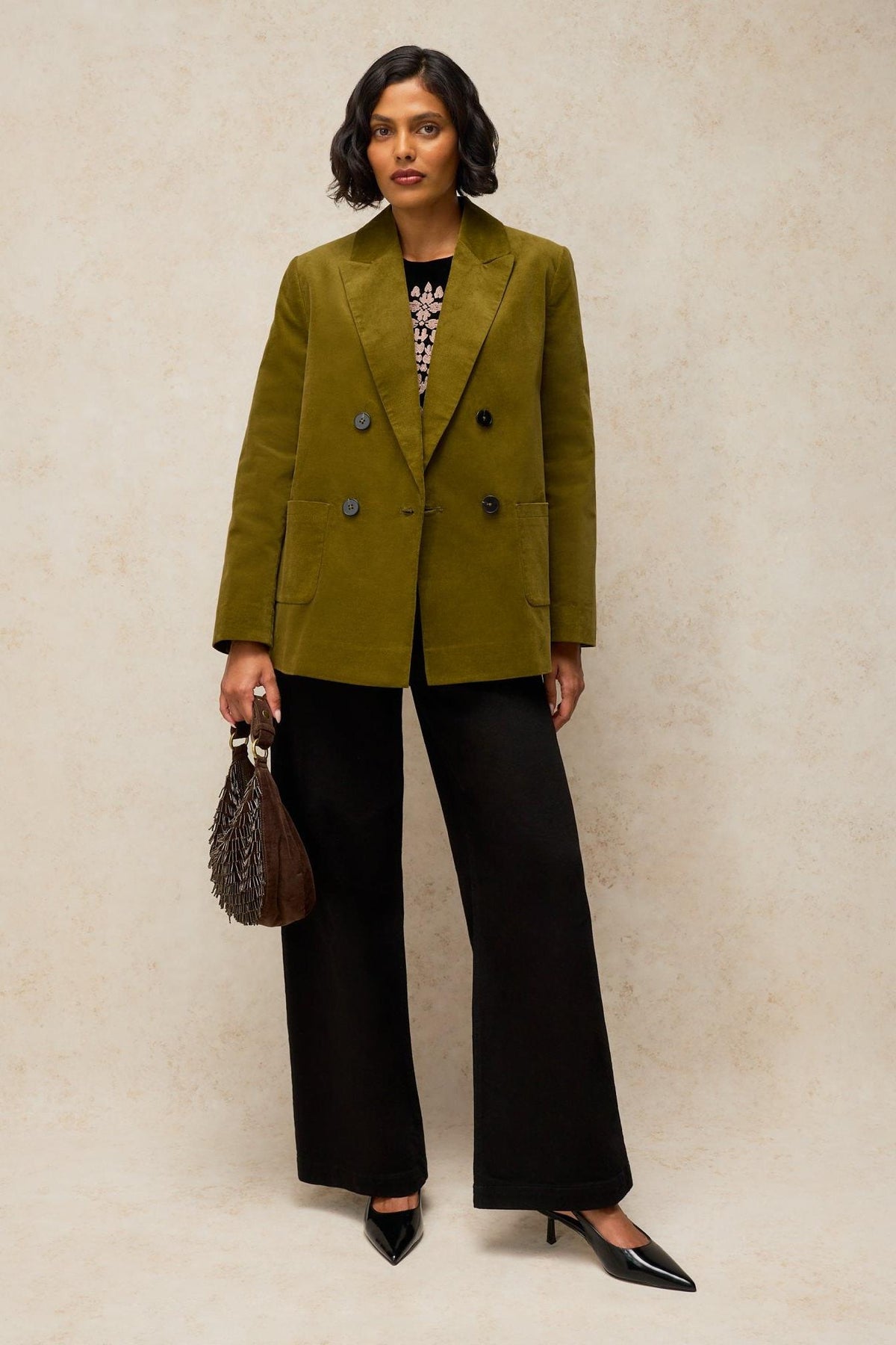 A woman wearing a double-breasted green velvet blazer and black wide-leg trousers for office or evening wear.