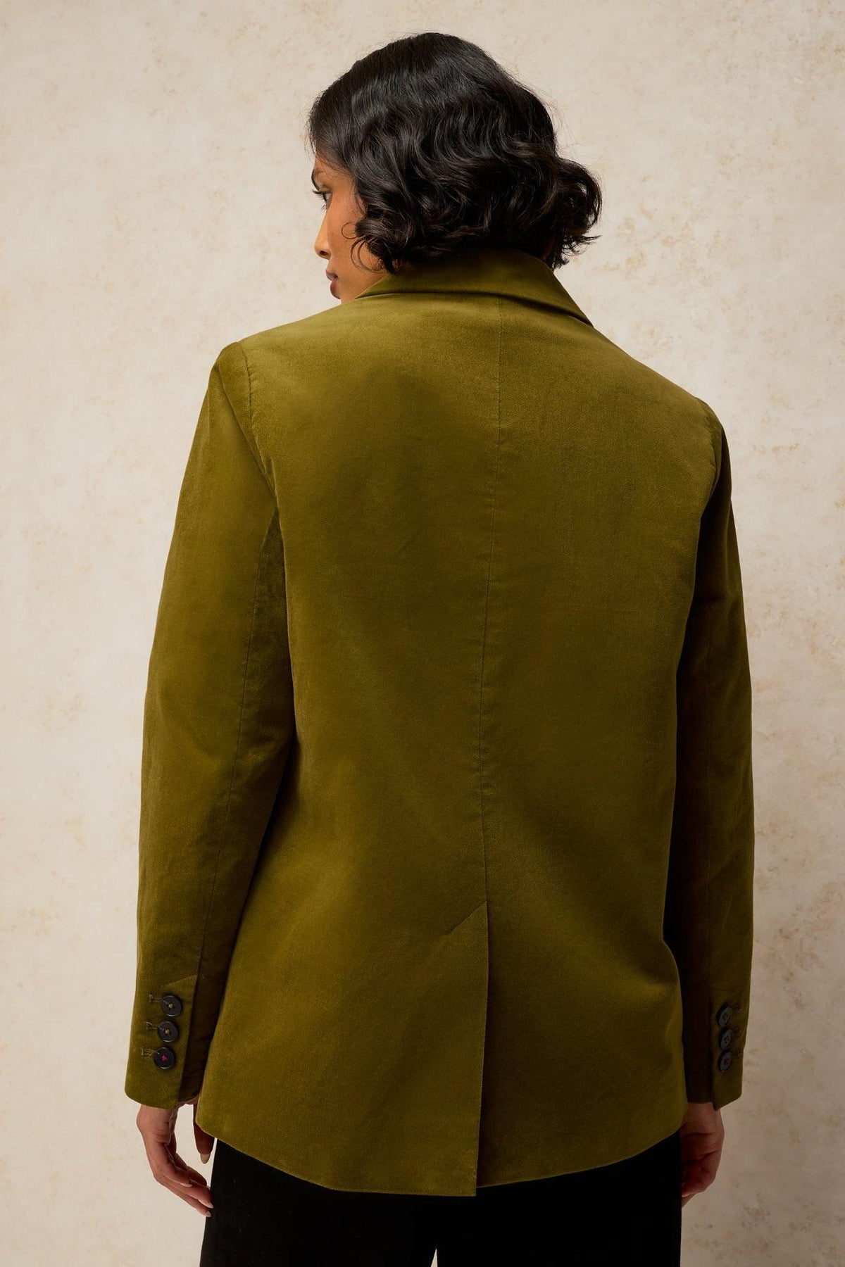 Woman seen from behind wearing a stylish green velvet blazer, suitable for office or evening wear.