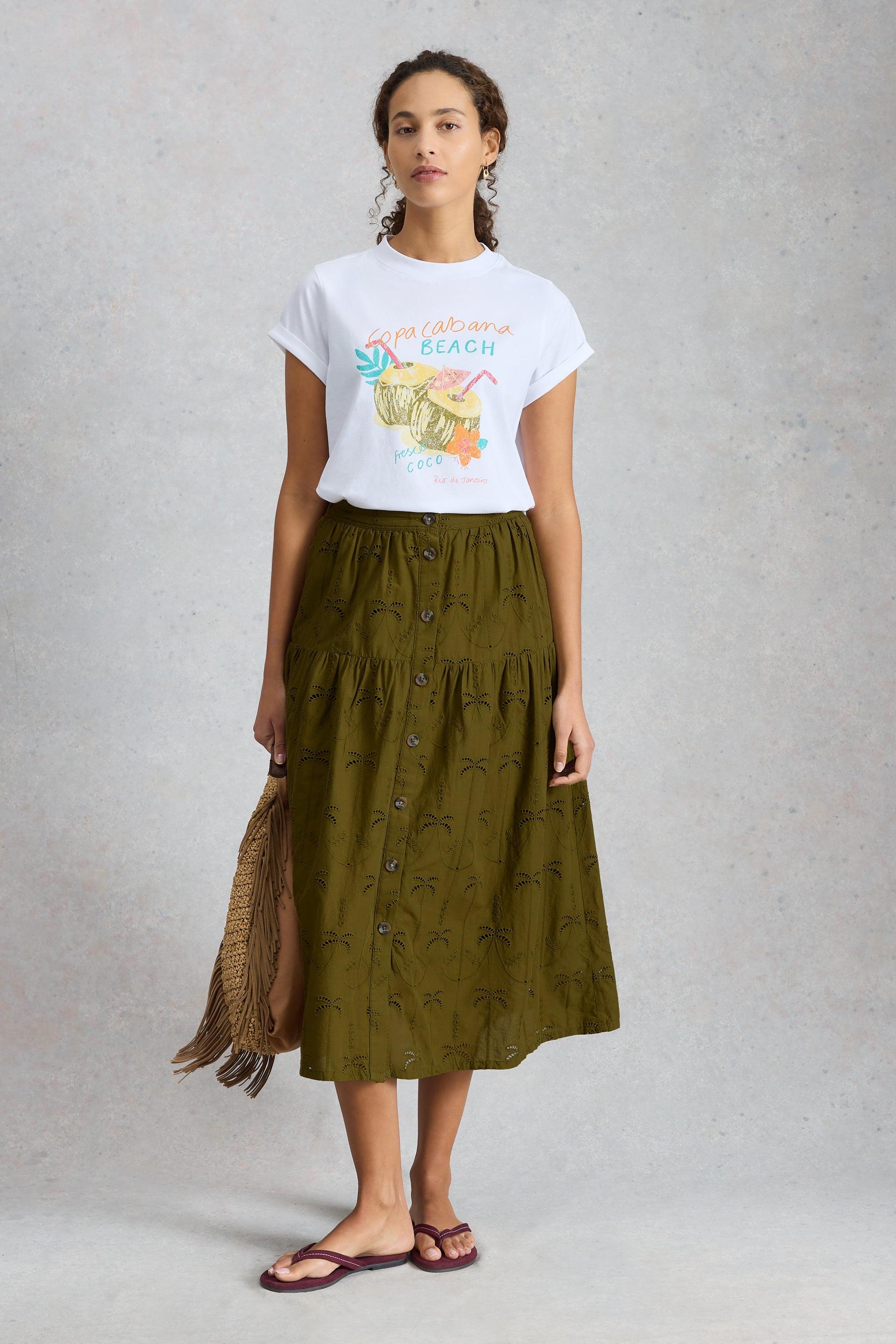 A woman modeling an olive green midi broderie skirt and a white graphic t-shirt.