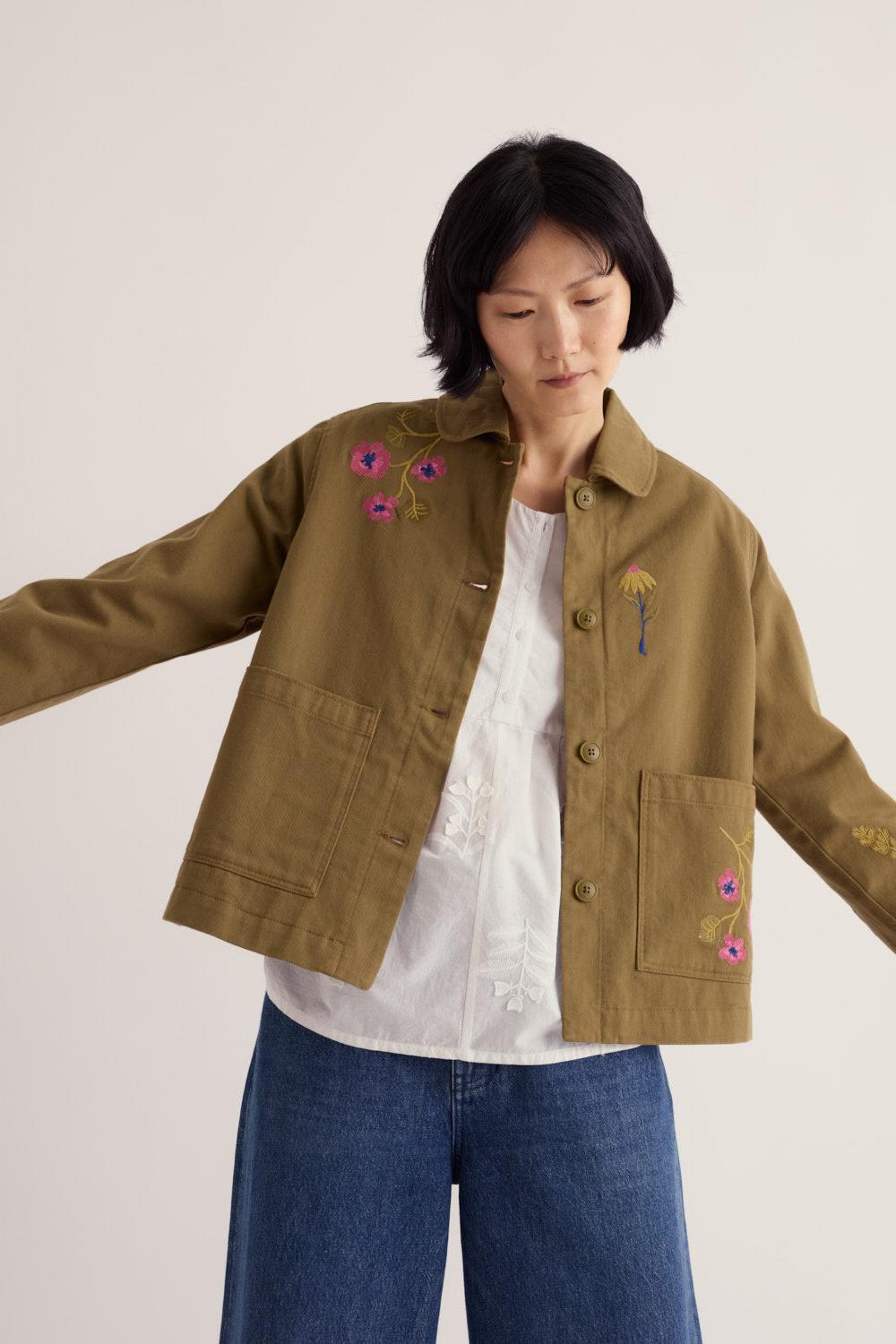A woman wearing a khaki organic cotton jacket with floral embroidery by Seasalt Cornwall.