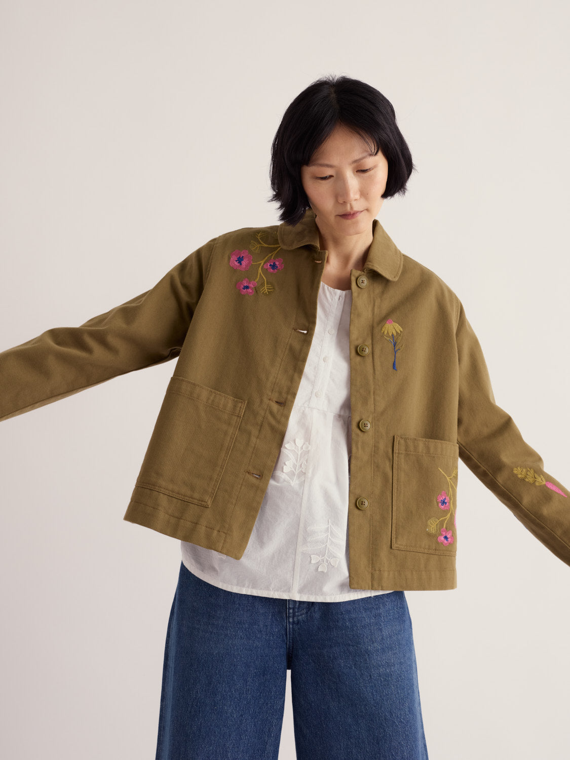 A woman wearing a khaki organic cotton jacket with floral embroidery by Seasalt Cornwall.
