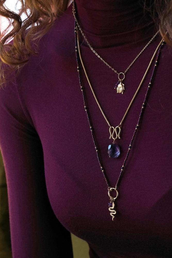 Close-up of a woman wearing a layered gold-plated necklace featuring an amethyst gemstone pendant.