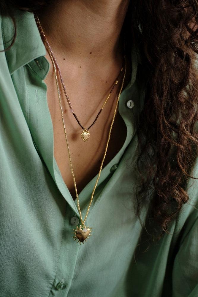 A woman wearing layered gold heart necklaces including a rose quartz gemstone piece.