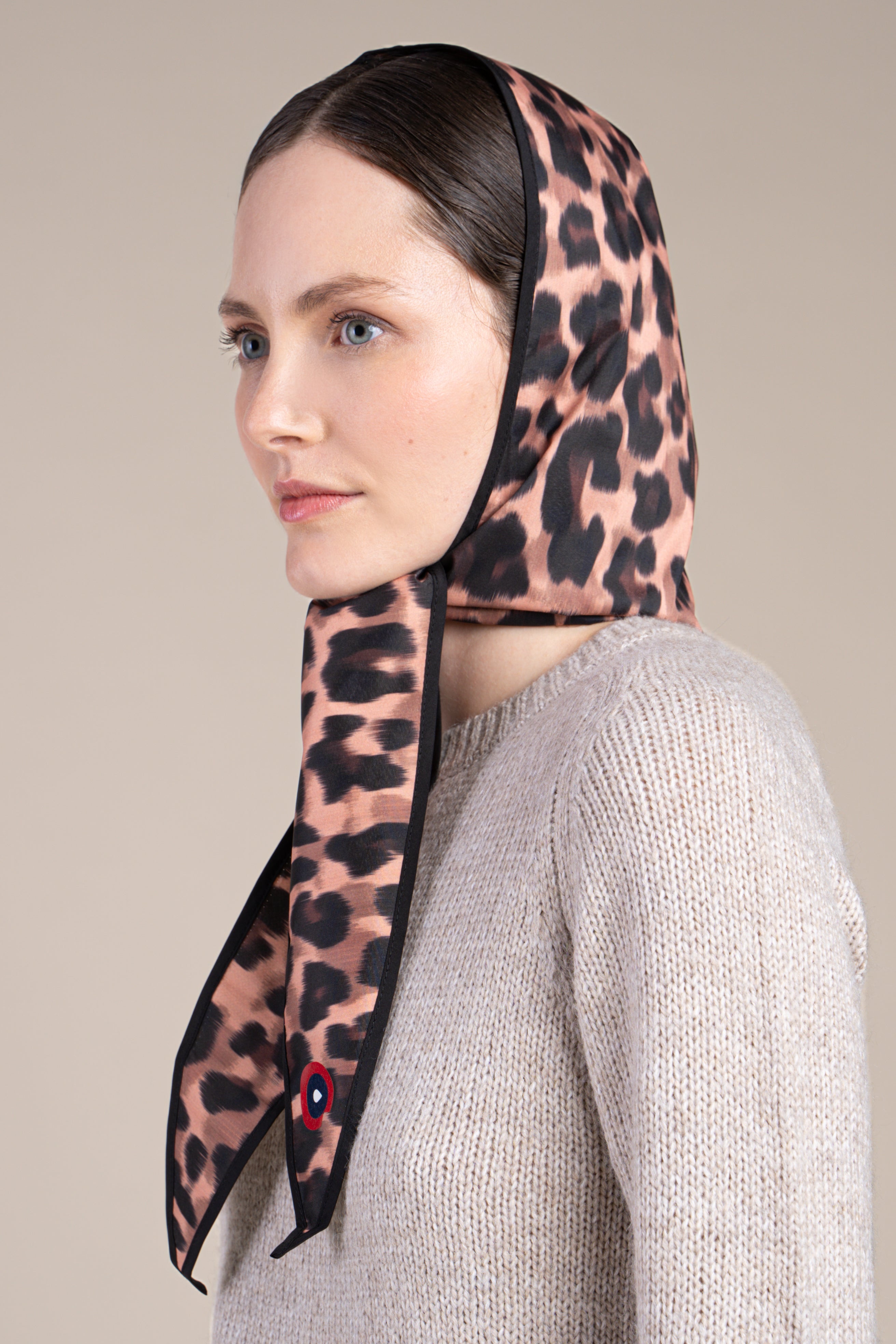 Woman wearing a leopard print waterproof head covering scarf against a neutral background