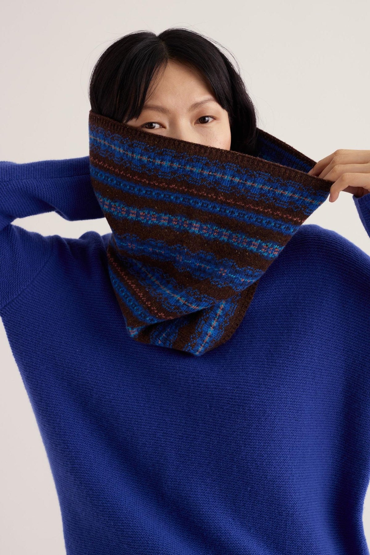 Woman wearing a patterned blue and brown Merino wool knit snood around her neck against a plain background.
