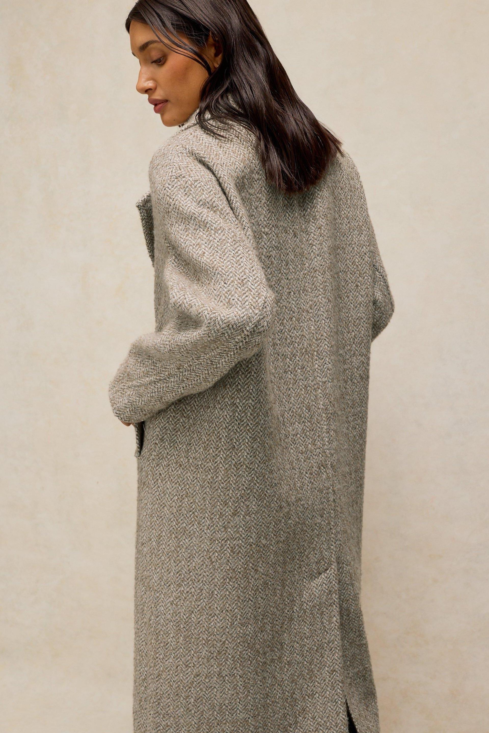 A woman from behind wearing a stylish natural colour wool coat against a neutral background.