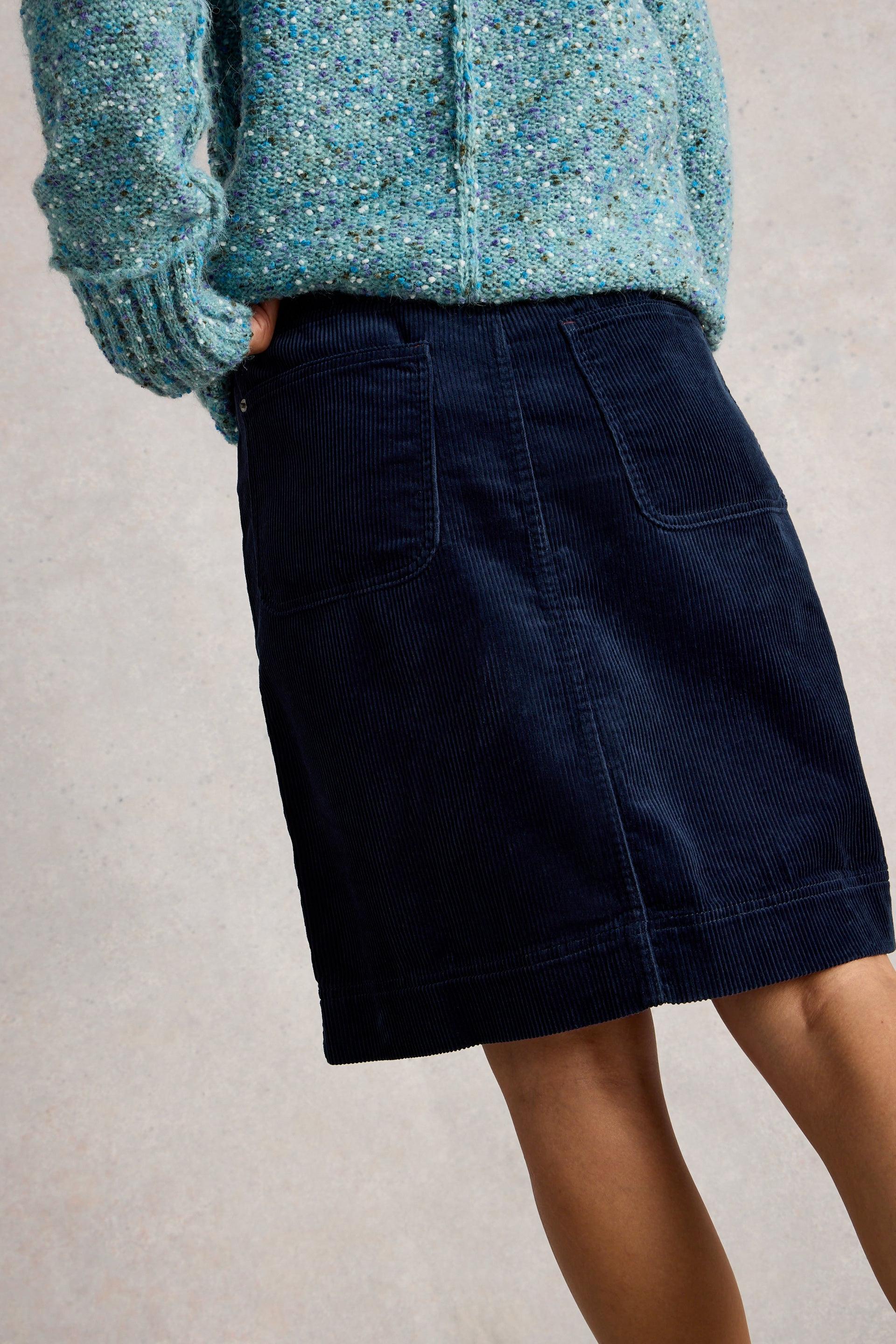 Person wearing a blue knitted sweater and dark denim skirt on a neutral background