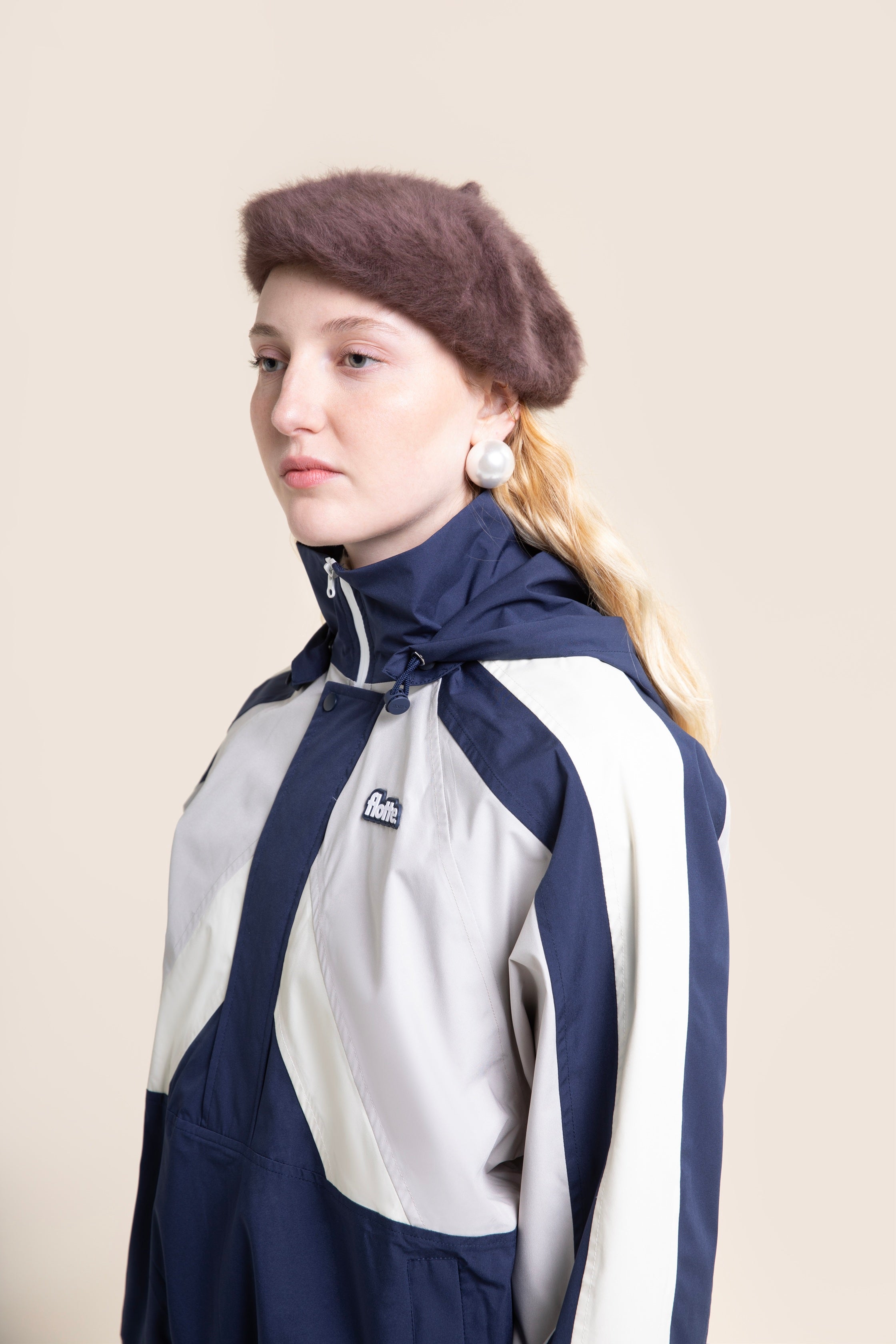 A woman wearing a stylish navy and white waterproof jacket and a brown beret against a light background.